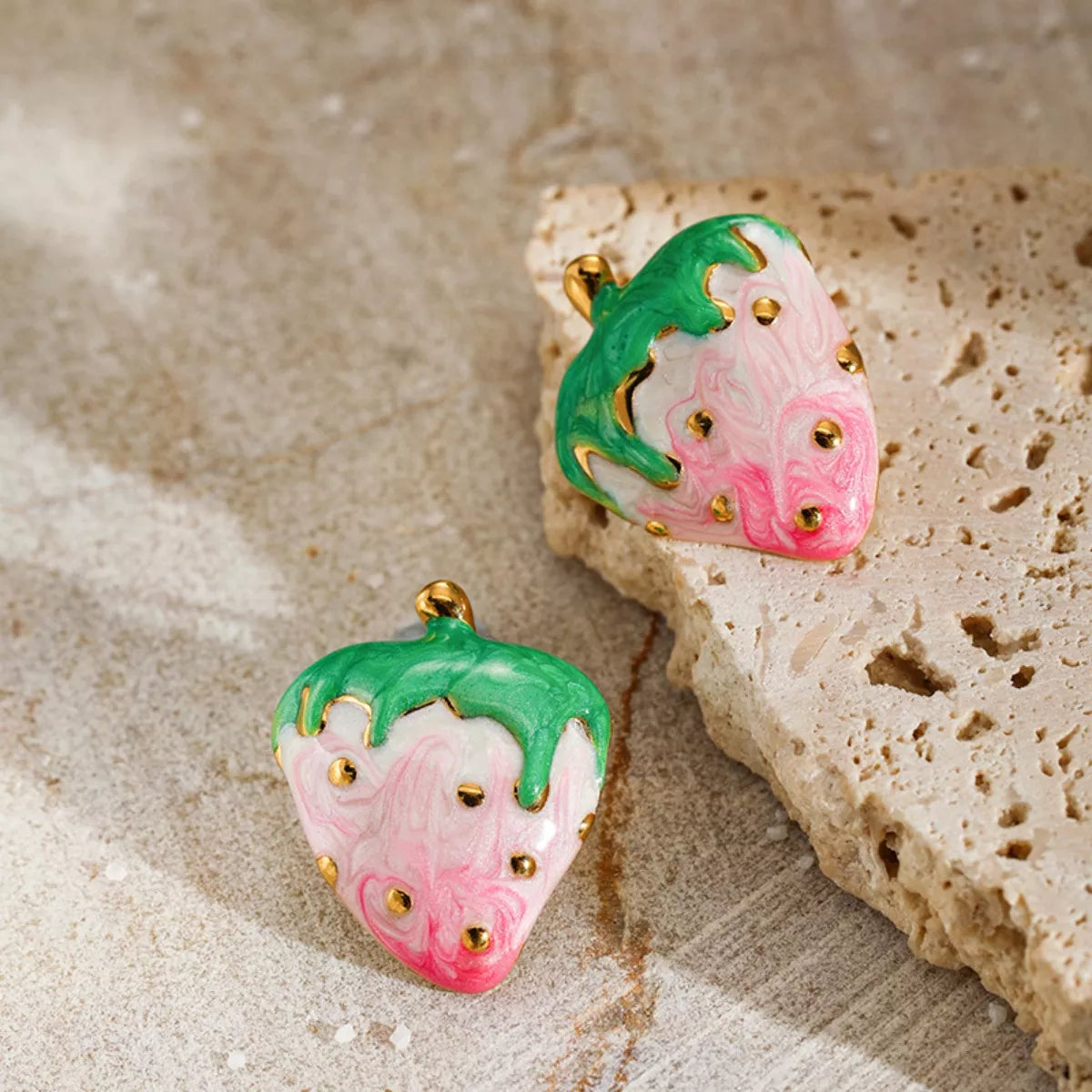 Pink and green strawberry stud earrings with gold accents on a neutral background