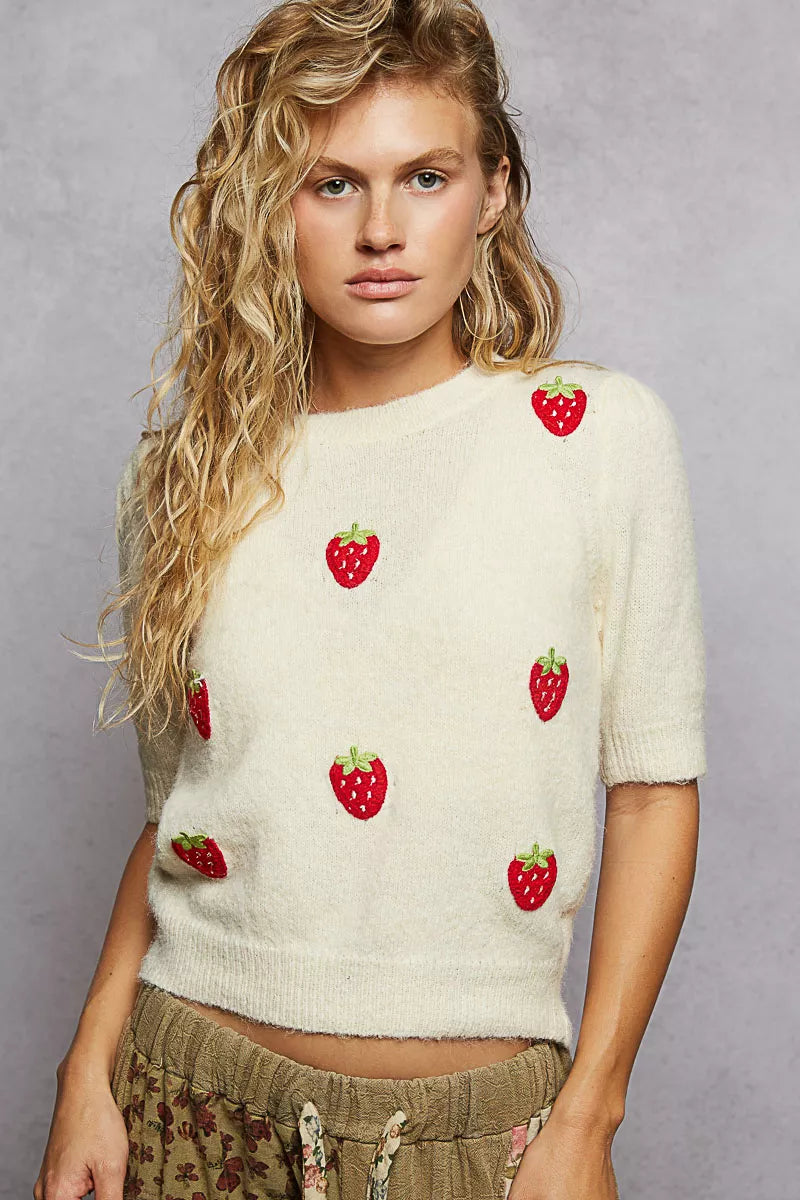 Cream knit sweater with embroidered red strawberry patches and round neckline.