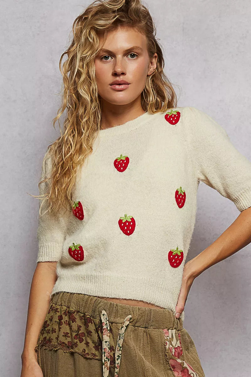 Cream knit sweater with embroidered red strawberry patches and round neckline.