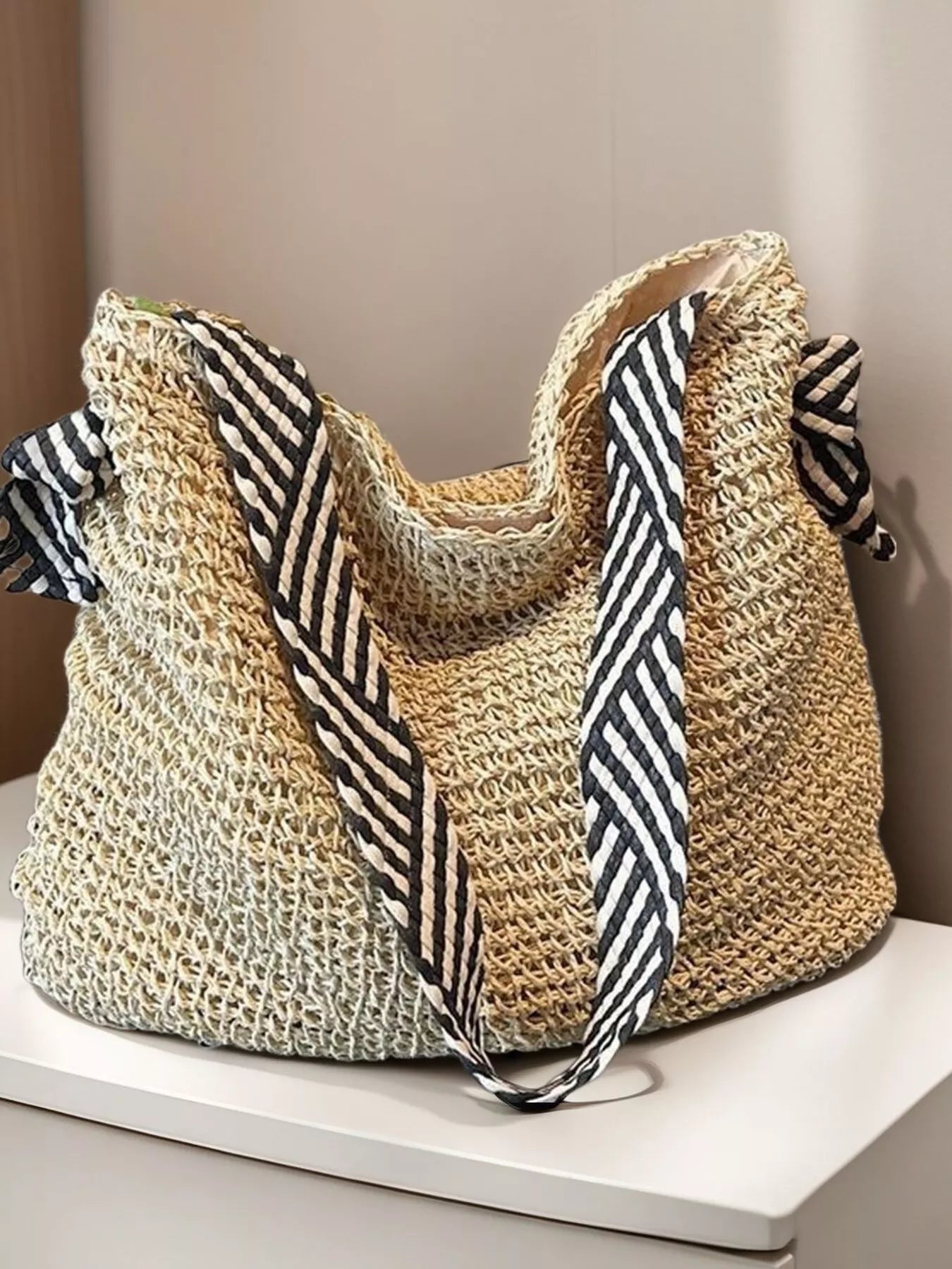 Large woven straw tote bag with black-and-white striped handles, displayed on a white table.