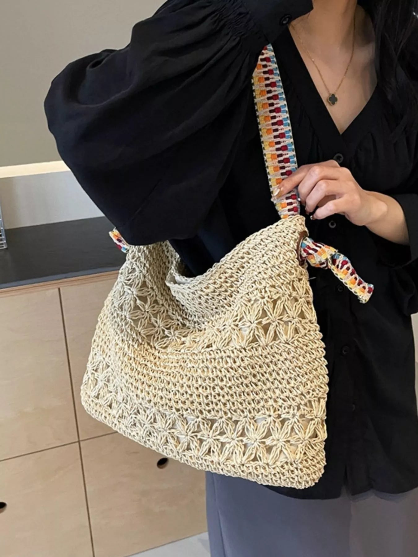 Large woven straw tote bag with black-and-white striped handles, displayed on a white table.