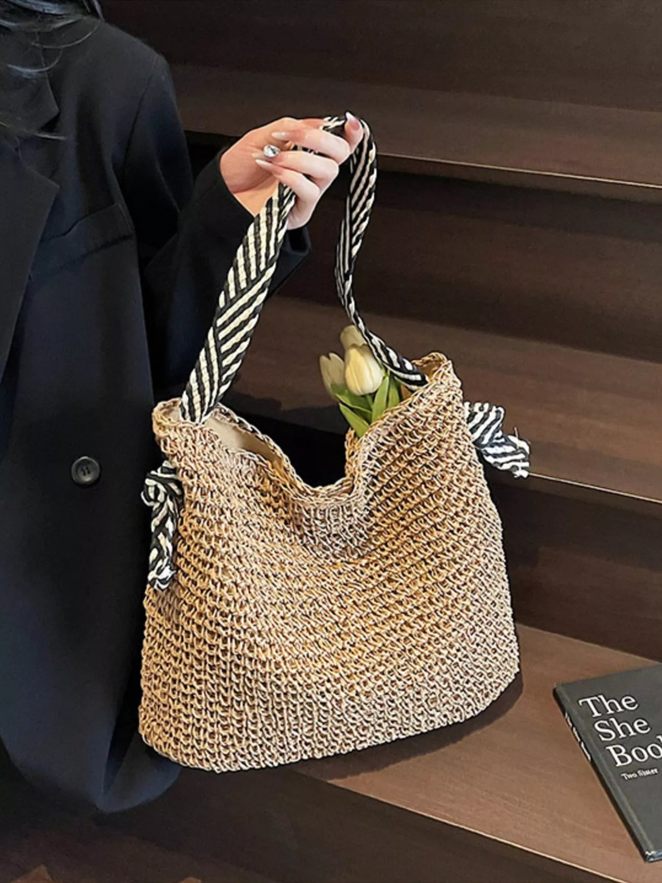 Large woven straw tote bag with black-and-white striped handles, displayed on a white table.