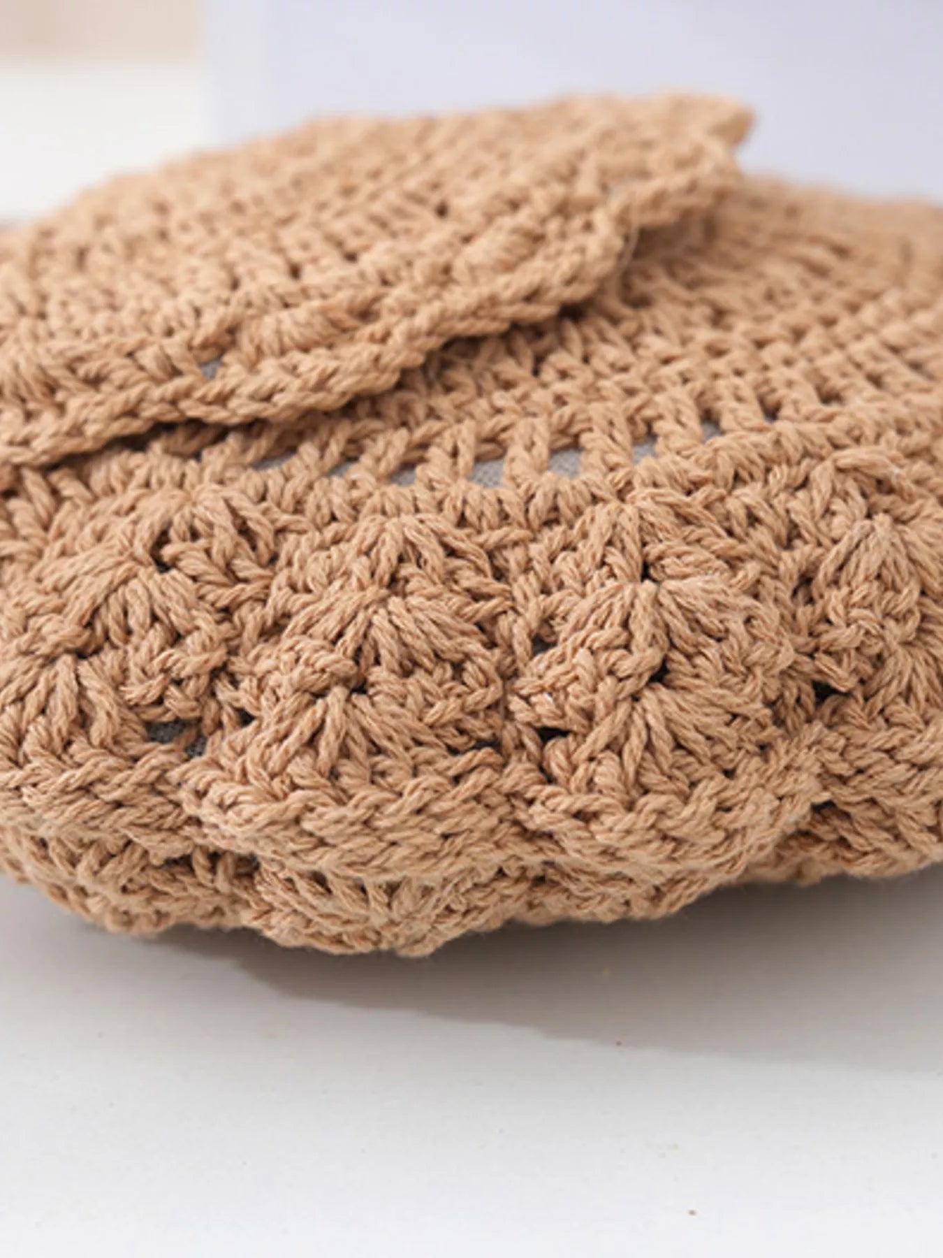 Small round crochet crossbody bag in natural beige cotton thread with scalloped edges and a flap closure.