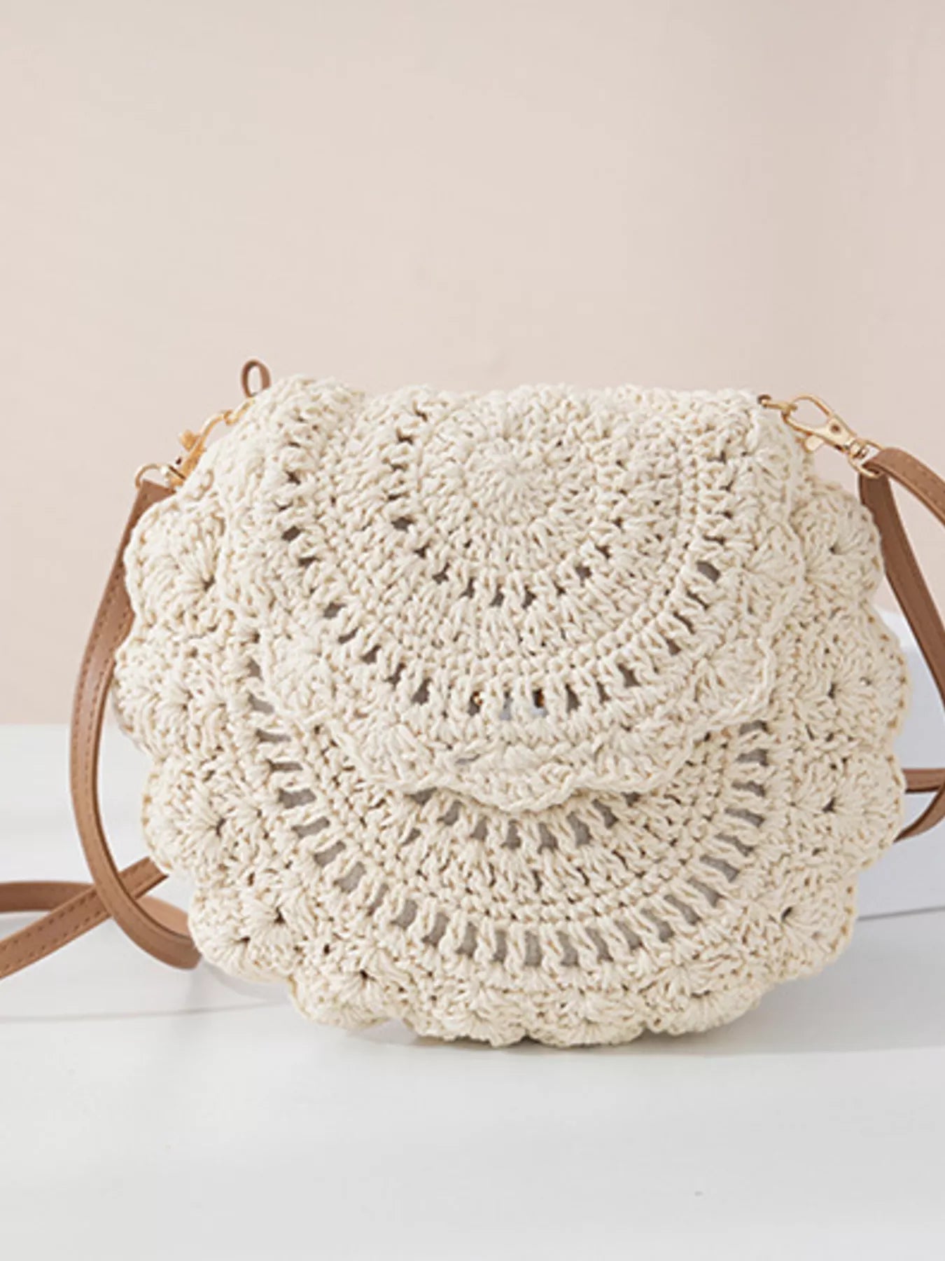 Small round crochet crossbody bag in white cotton thread with scalloped edges and a flap closure.