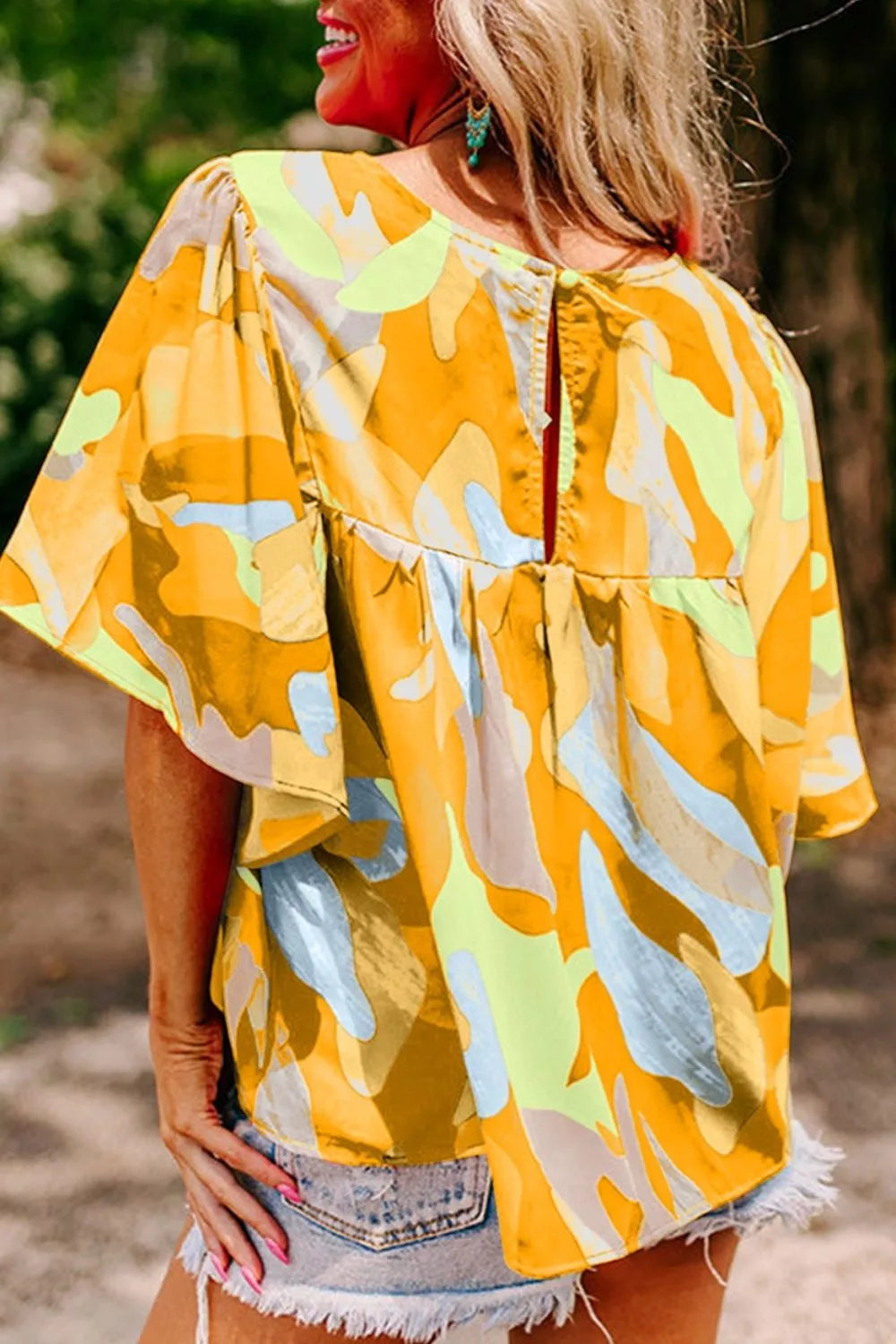Bright abstract print flutter sleeve top with a relaxed fit, tied detail, and breezy summer style paired with denim shorts.