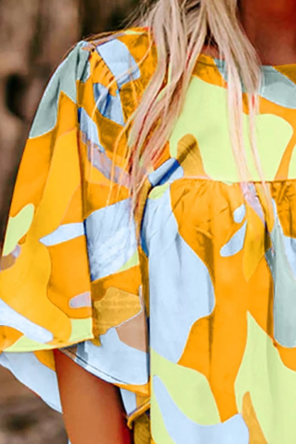 Bright abstract print flutter sleeve top with a relaxed fit, tied detail, and breezy summer style paired with denim shorts.