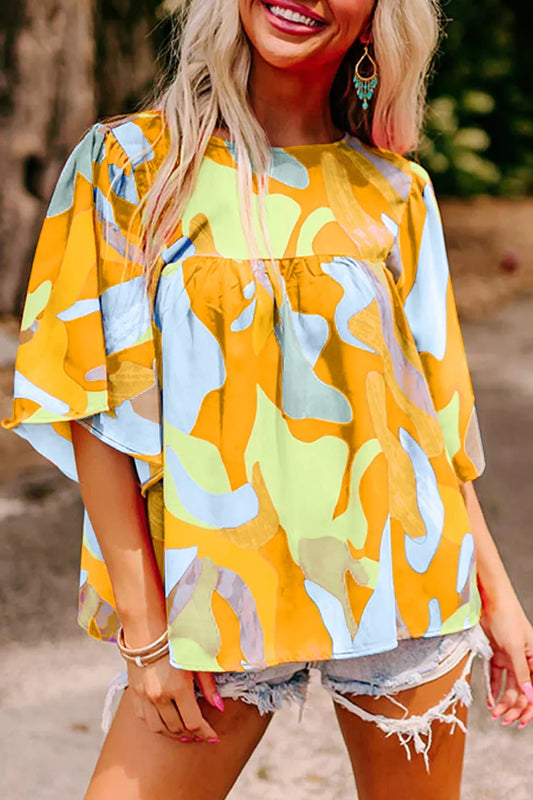 Bright abstract print flutter sleeve top with a relaxed fit, tied detail, and breezy summer style paired with denim shorts.