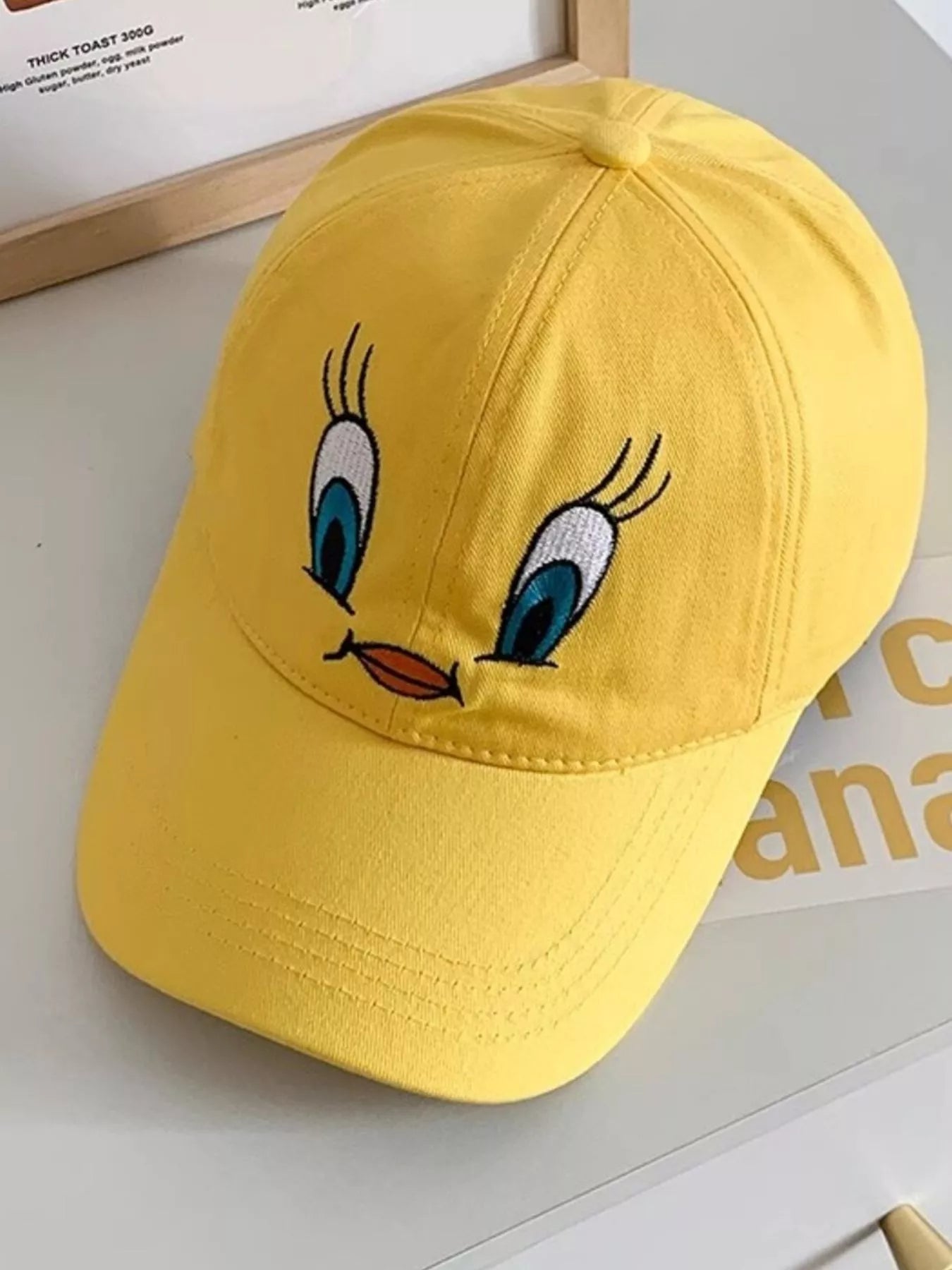 Bright yellow cotton baseball cap with an embroidered bird face design on the front.