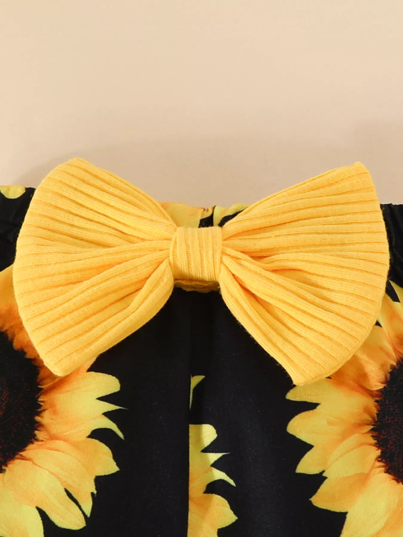 Baby outfit featuring a yellow ruffled romper, sunflower bell-bottom pants, and matching sunflower bow headband displayed flat with floral accents.