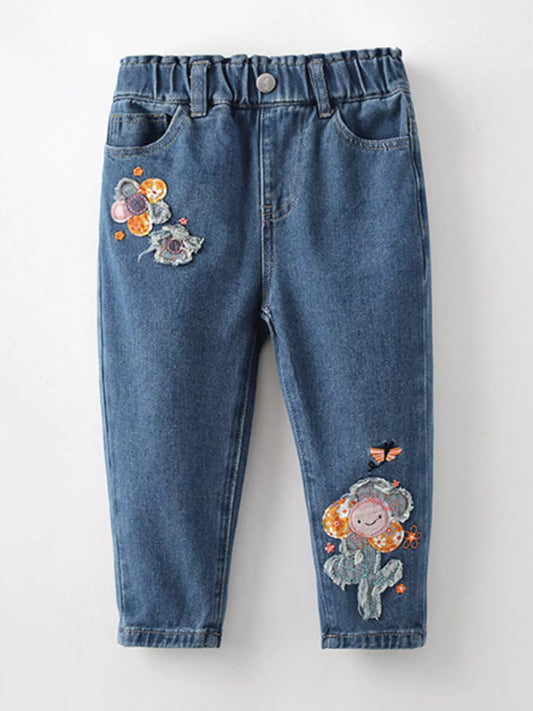 Close-up of embroidered flowers and happy face patch on children’s jeans