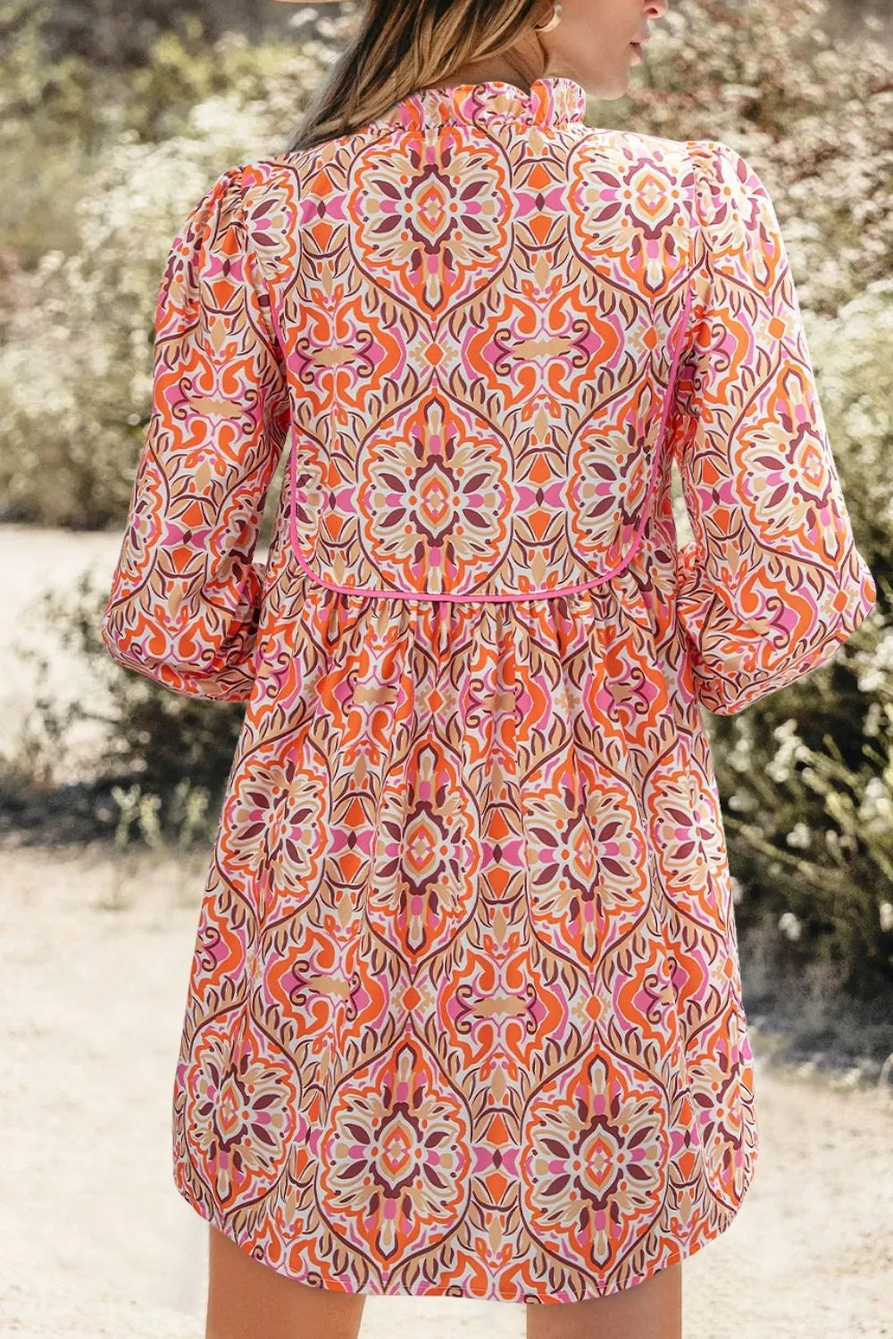 Colorful mosaic-print mini dress with frilled neckline and long sleeves in pink, orange, and coral tones.