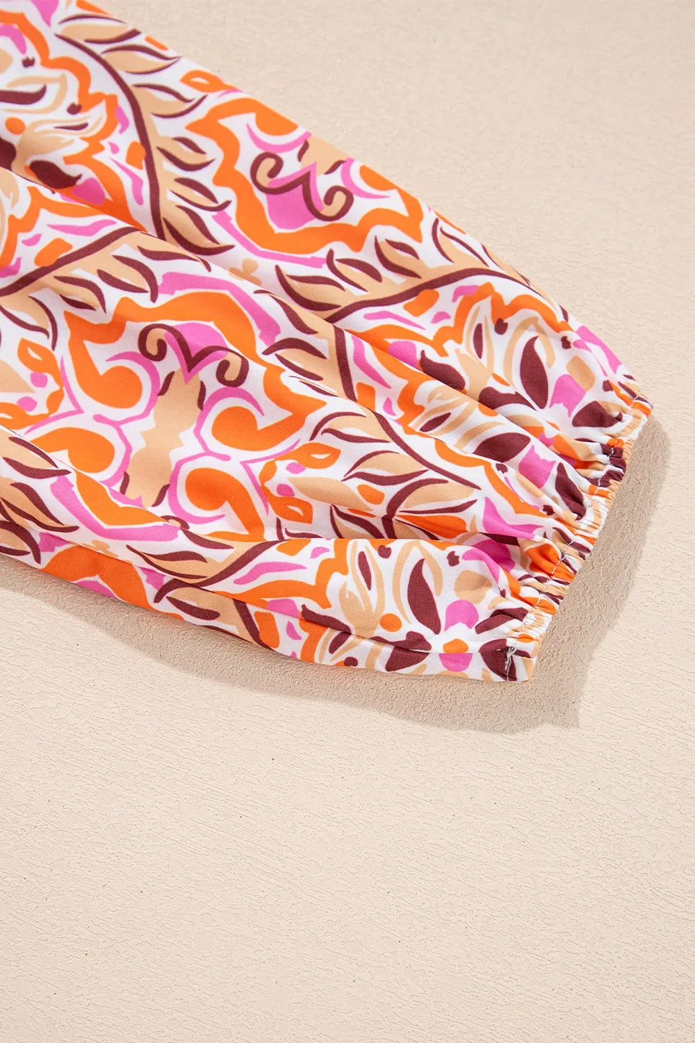 Colorful mosaic-print mini dress with frilled neckline and long sleeves in pink, orange, and coral tones.