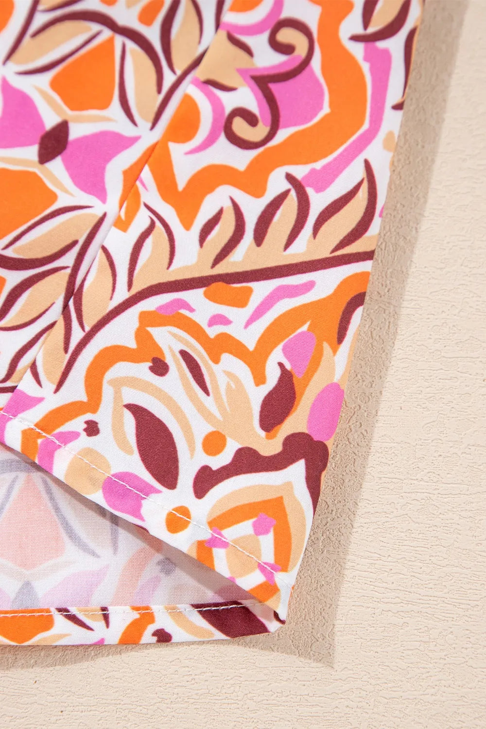 Colorful mosaic-print mini dress with frilled neckline and long sleeves in pink, orange, and coral tones.