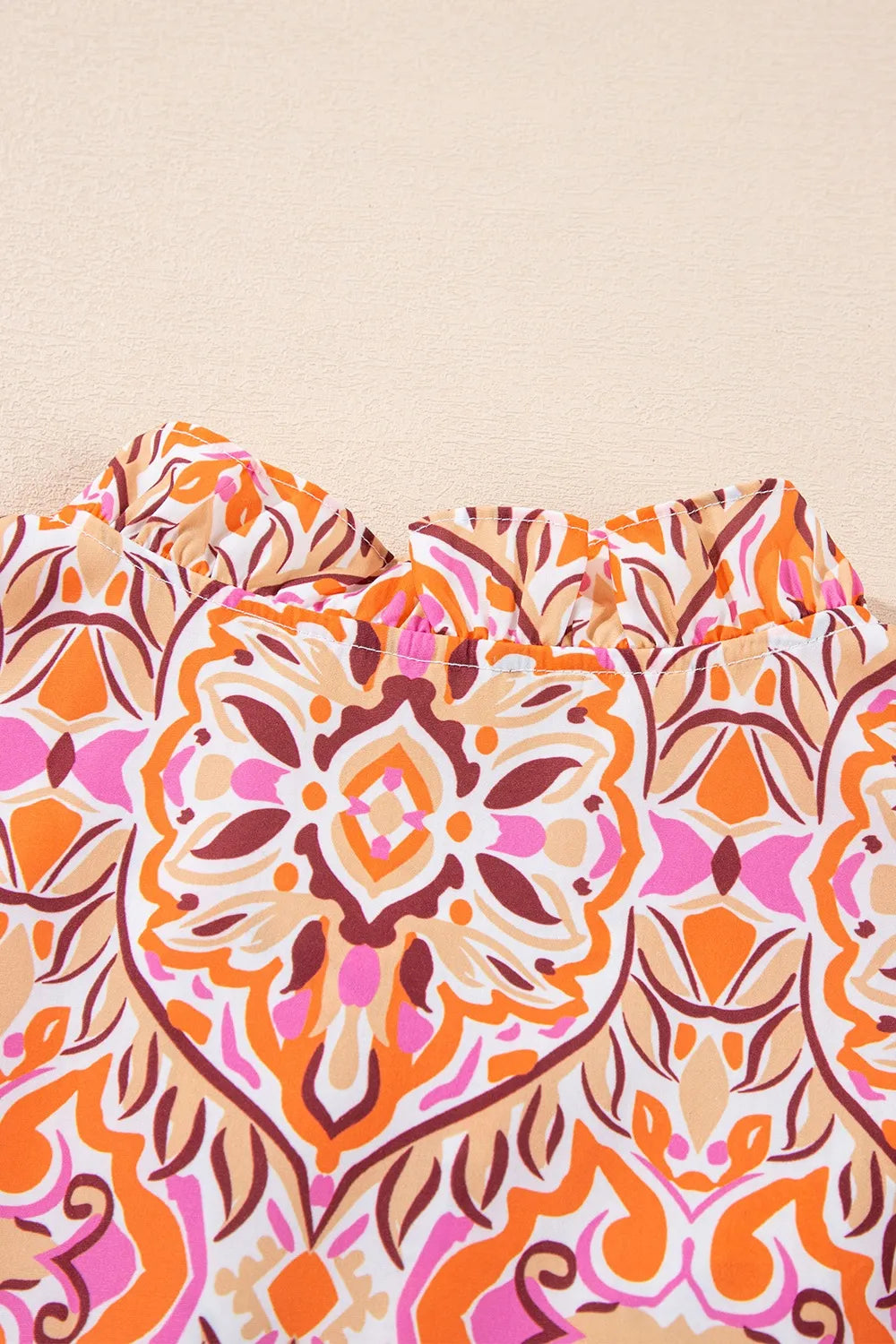 Colorful mosaic-print mini dress with frilled neckline and long sleeves in pink, orange, and coral tones.