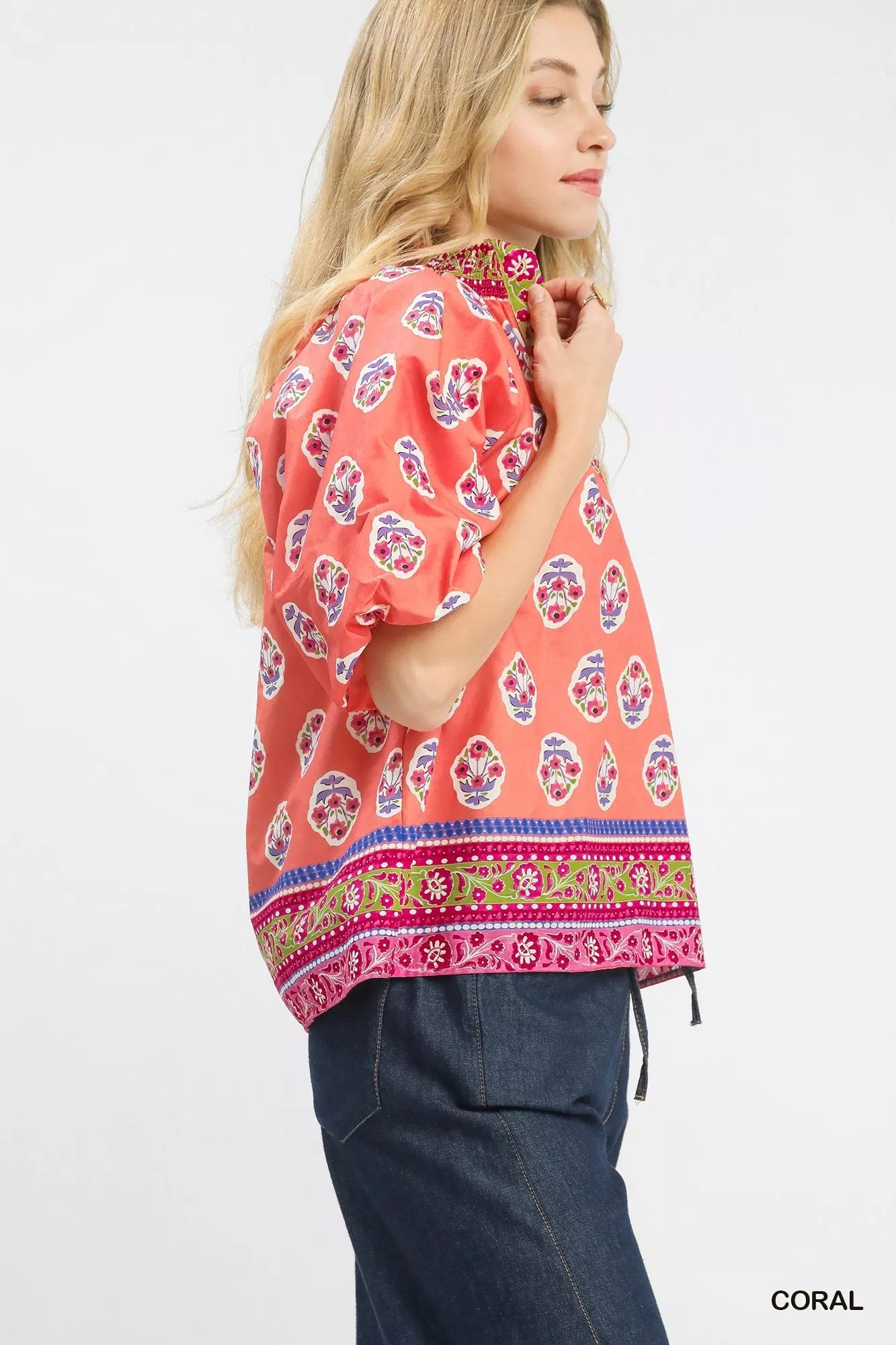 Woman wearing a coral boho border print peasant top with puff sleeves and a contrast V neckline