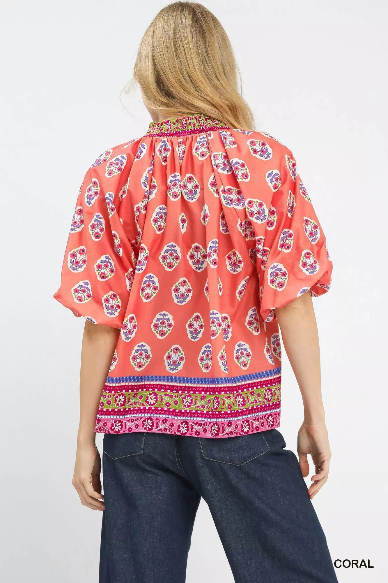 Woman wearing a coral boho border print peasant top with puff sleeves and a contrast V neckline