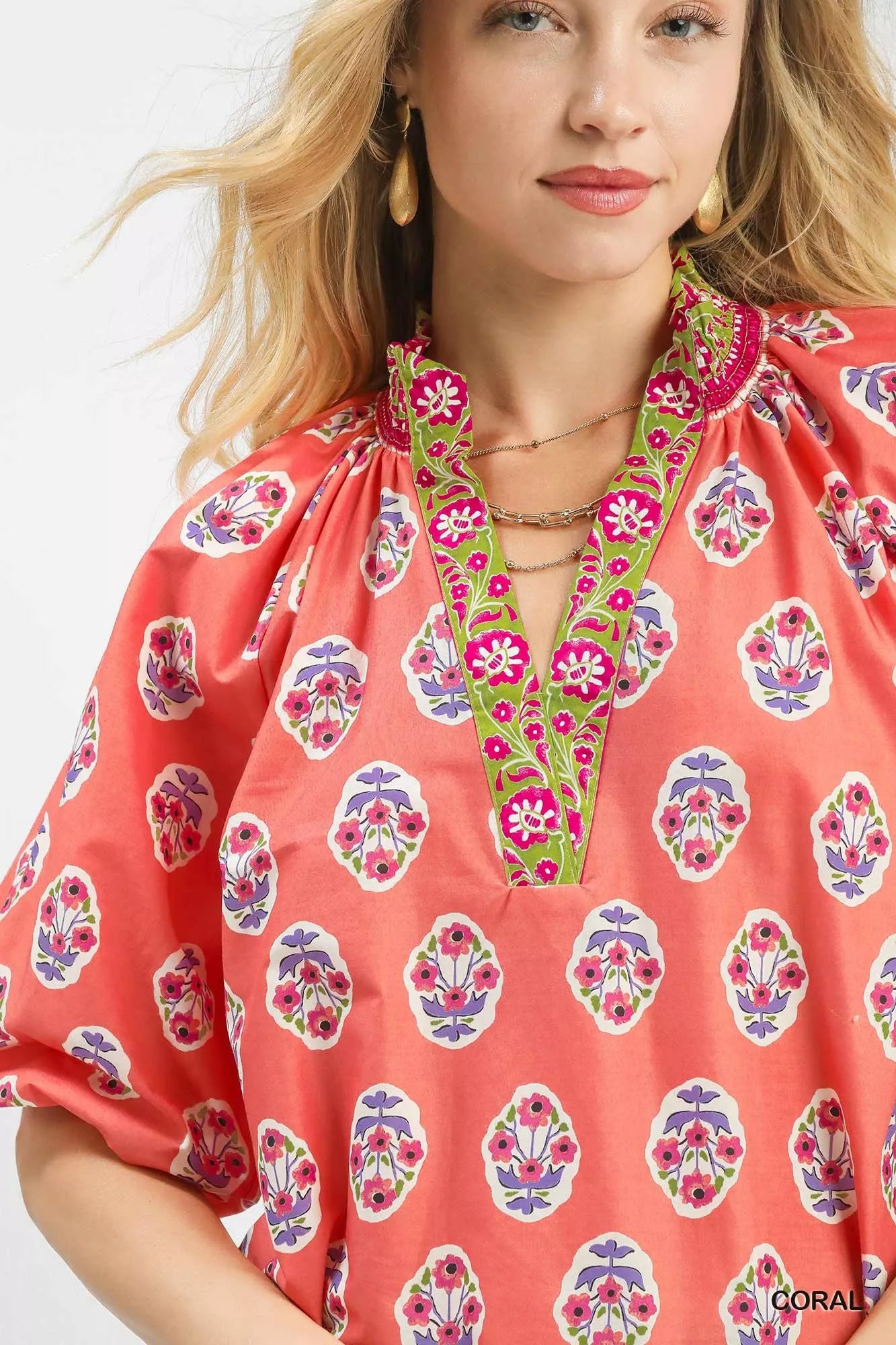 Woman wearing a coral boho border print peasant top with puff sleeves and a contrast V neckline