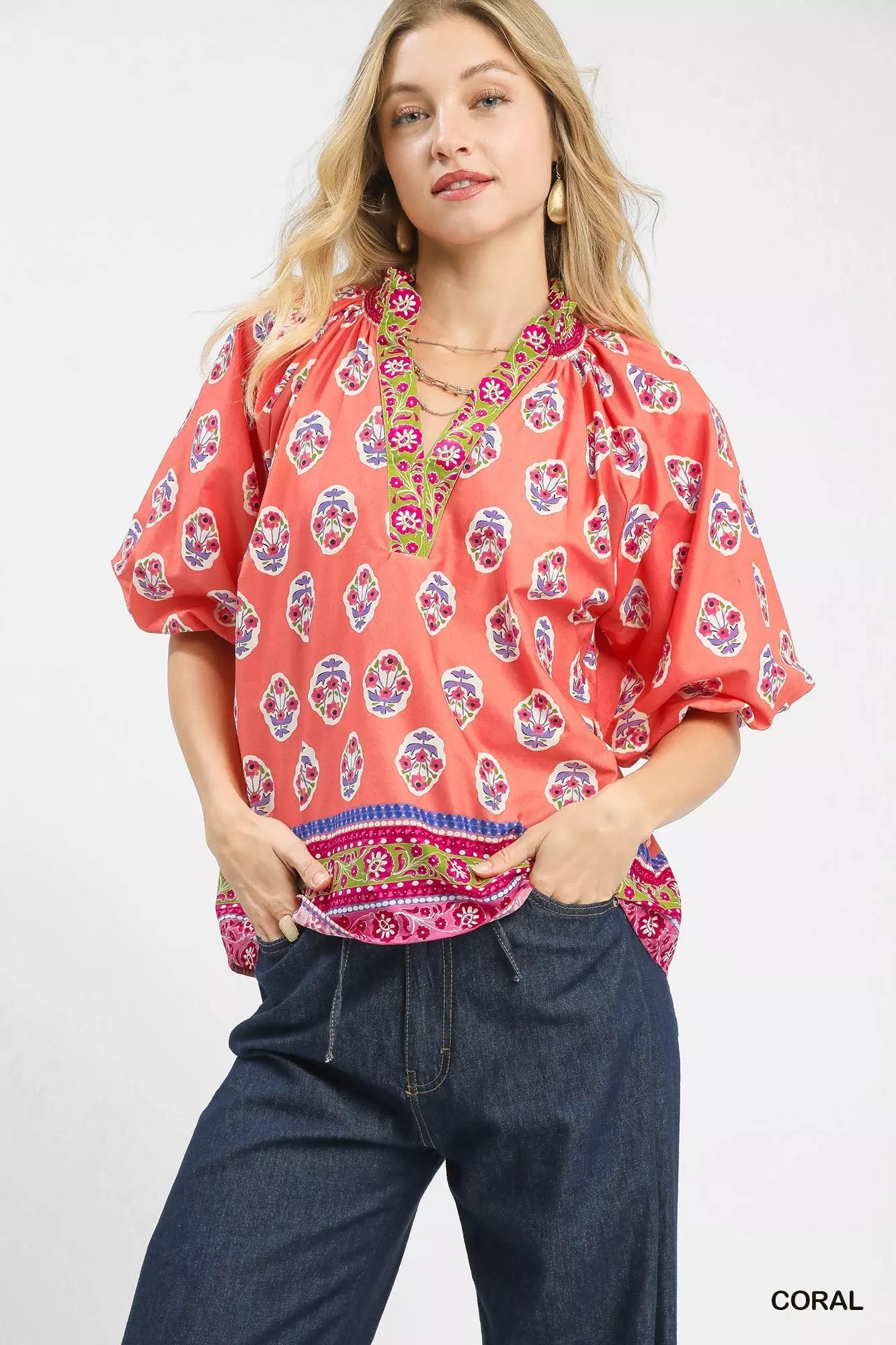 Woman wearing a coral boho border print peasant top with puff sleeves and a contrast V neckline