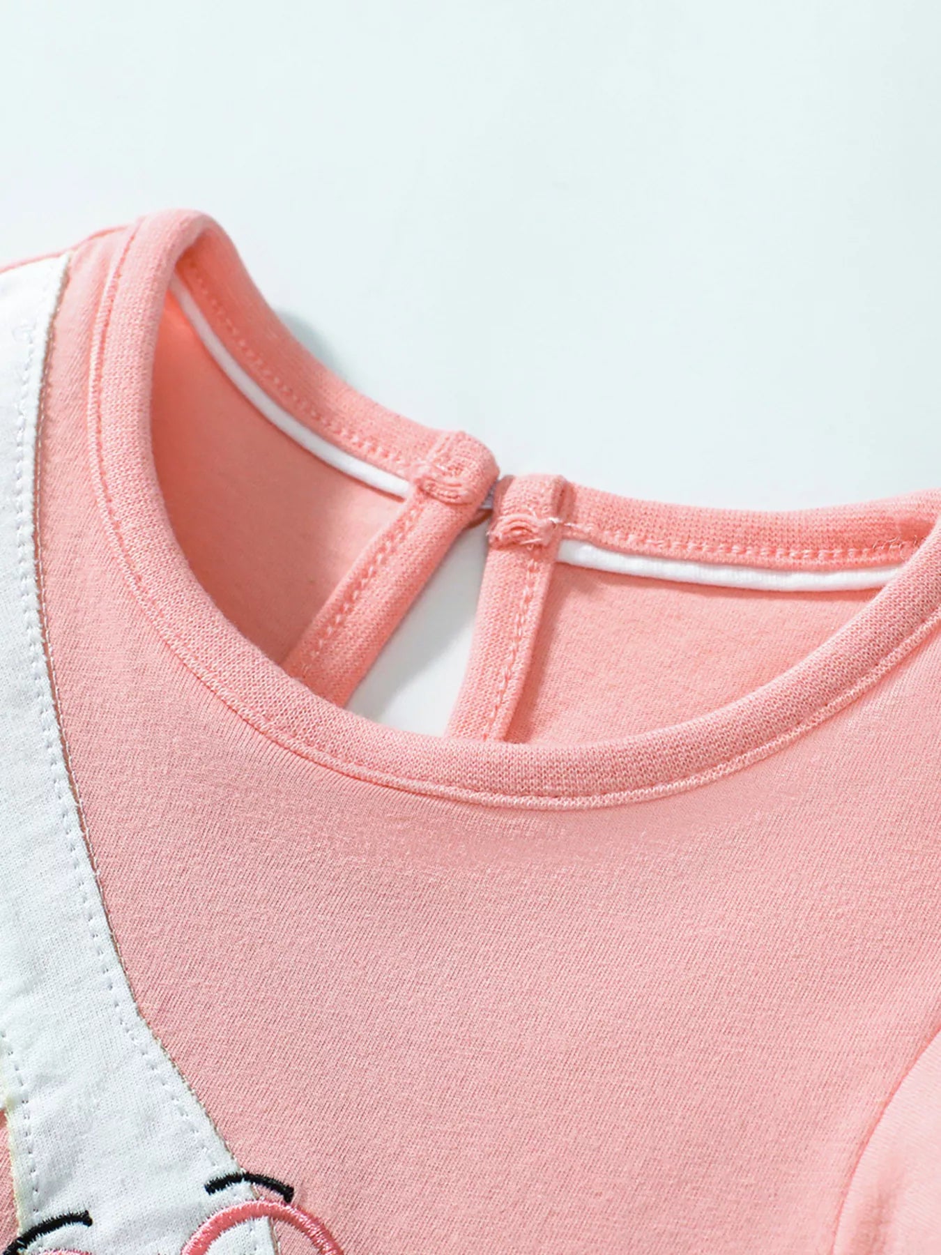 Pink girls dress with flutter sleeves and playful bird detail styled indoors