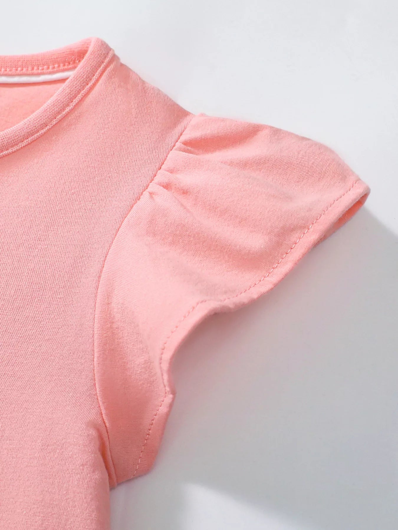 Pink girls dress with flutter sleeves and playful bird detail styled indoors