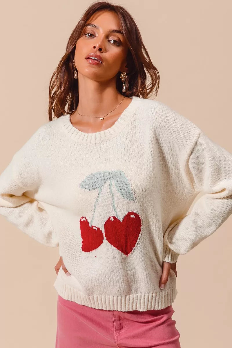 Cream knit sweater with red heart-shaped cherry design on model