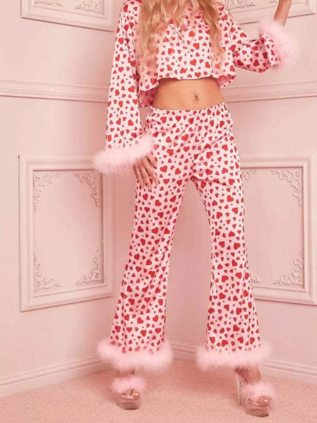 Woman wearing pink and red heart print pajama set with feather trim on sleeves and pants