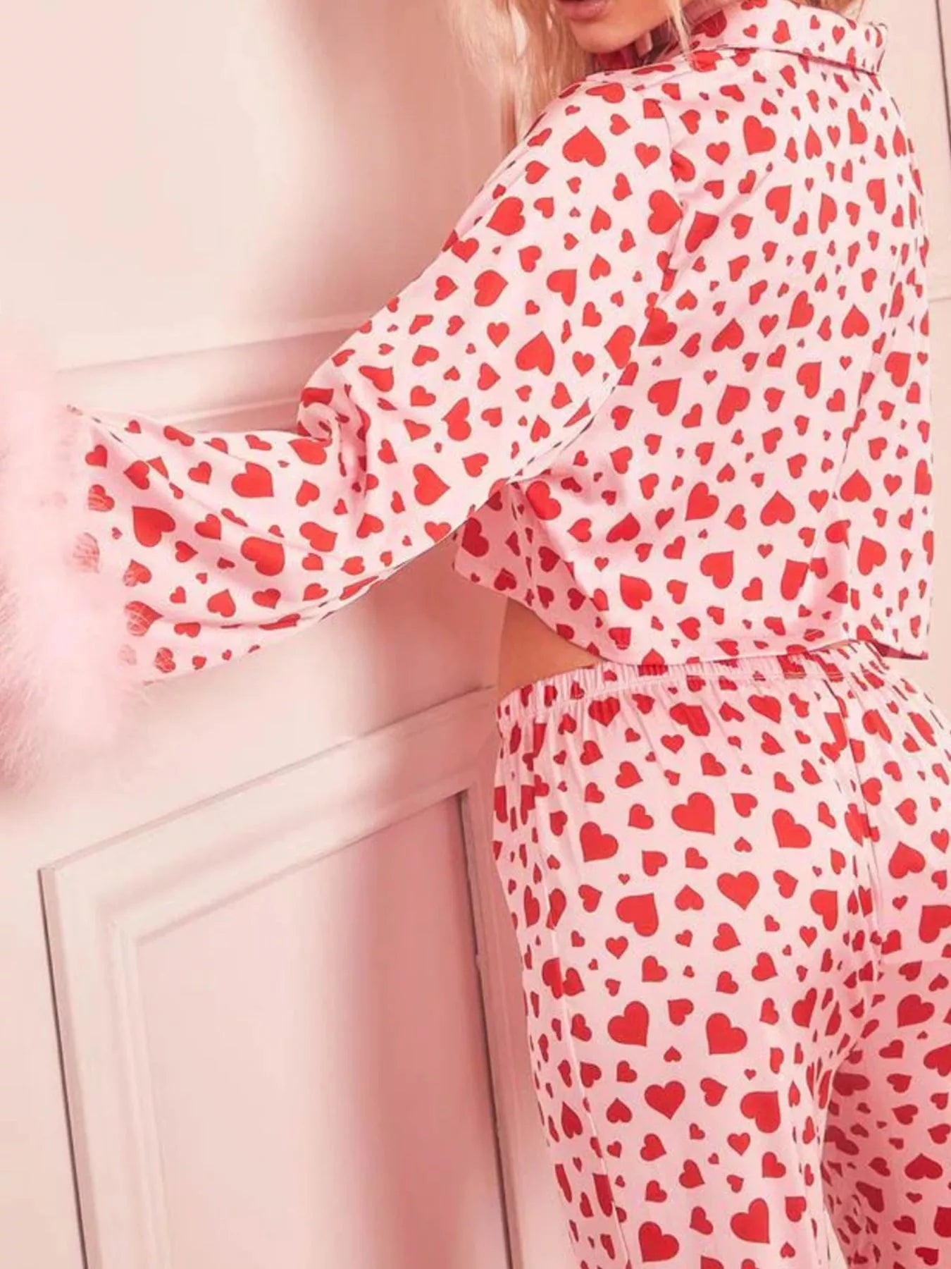 Woman wearing pink and red heart print pajama set with feather trim on sleeves and pants