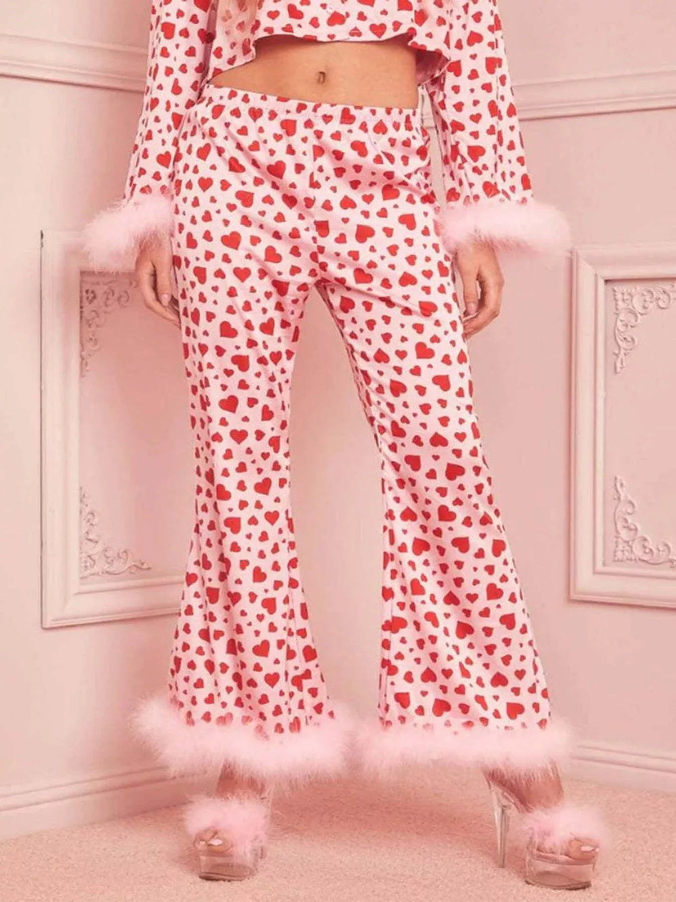 Woman wearing pink and red heart print pajama set with feather trim on sleeves and pants