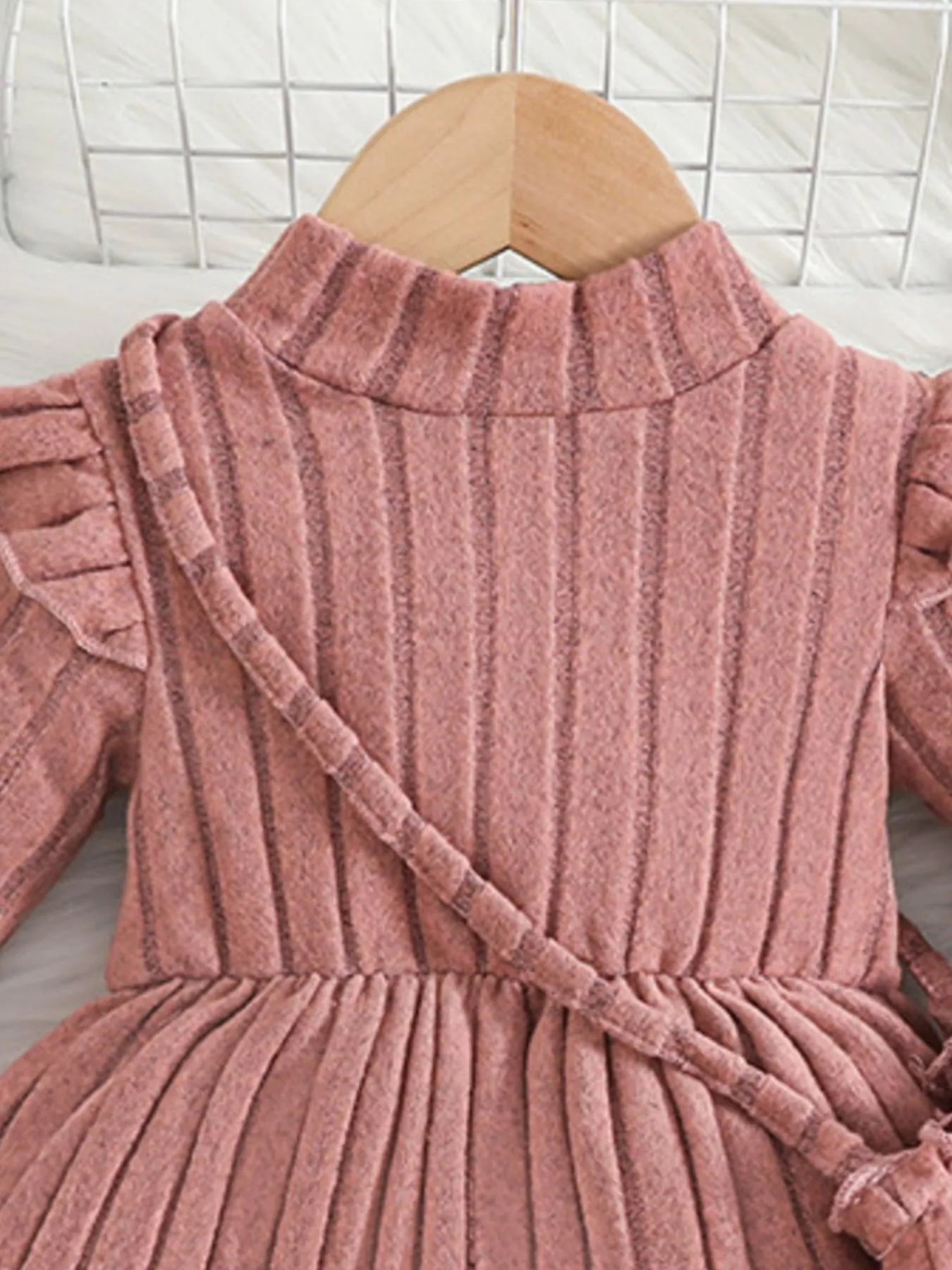 Soft pink ribbed sweater dress for girls featuring ruffled sleeves and matching purse, laid flat beside floral decor and accessories.