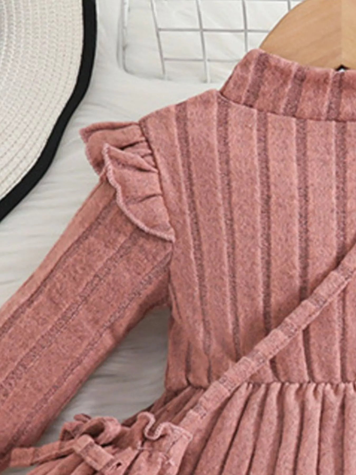 Soft pink ribbed sweater dress for girls featuring ruffled sleeves and matching purse, laid flat beside floral decor and accessories.