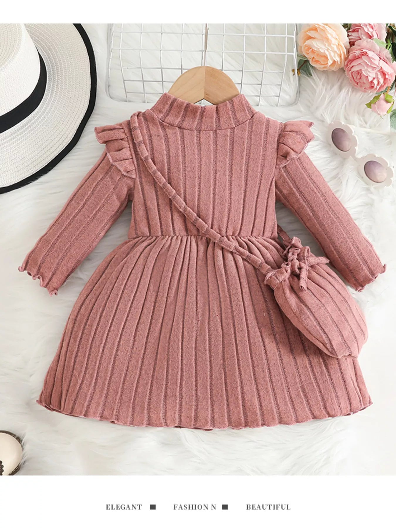 Soft pink ribbed sweater dress for girls featuring ruffled sleeves and matching purse, laid flat beside floral decor and accessories.