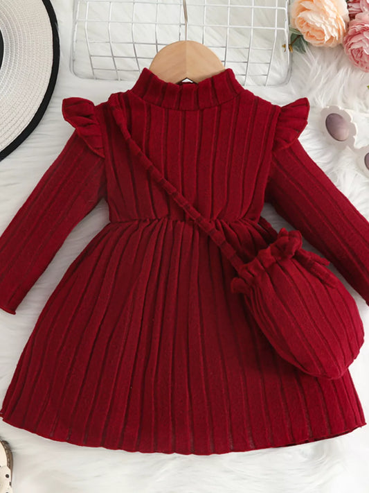 Red ribbed knit toddler dress with frilled shoulders and matching purse, displayed flat on white fur background with flowers and accessories.