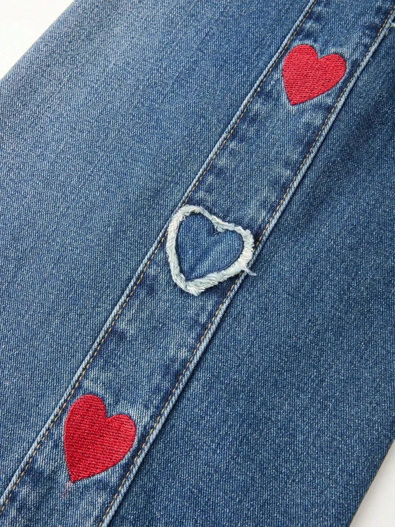 Relaxed denim pants with embroidered red and white heart details along the side panels, elastic waistband, and cuffed hems.