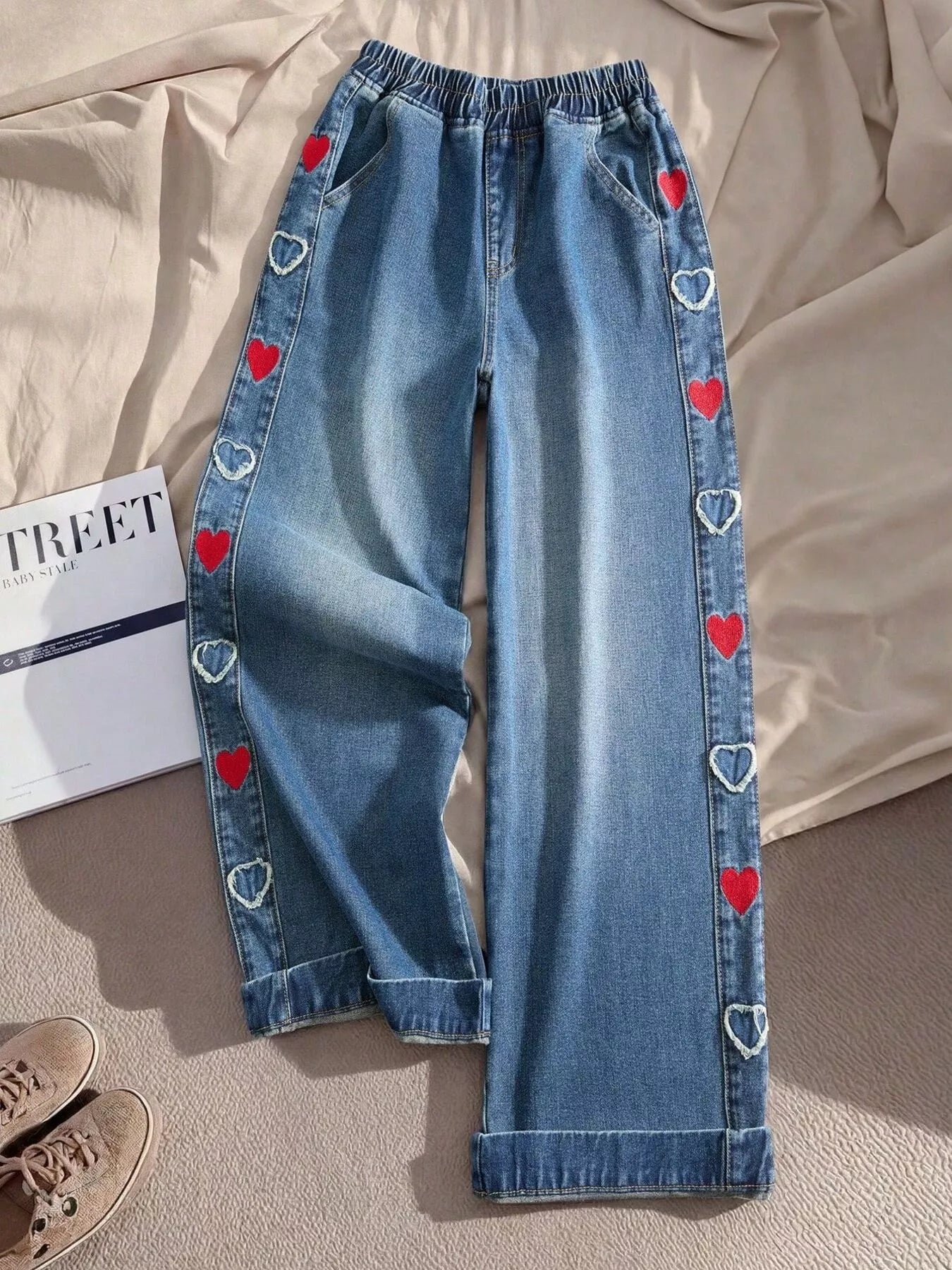 Relaxed denim pants with embroidered red and white heart details along the side panels, elastic waistband, and cuffed hems.