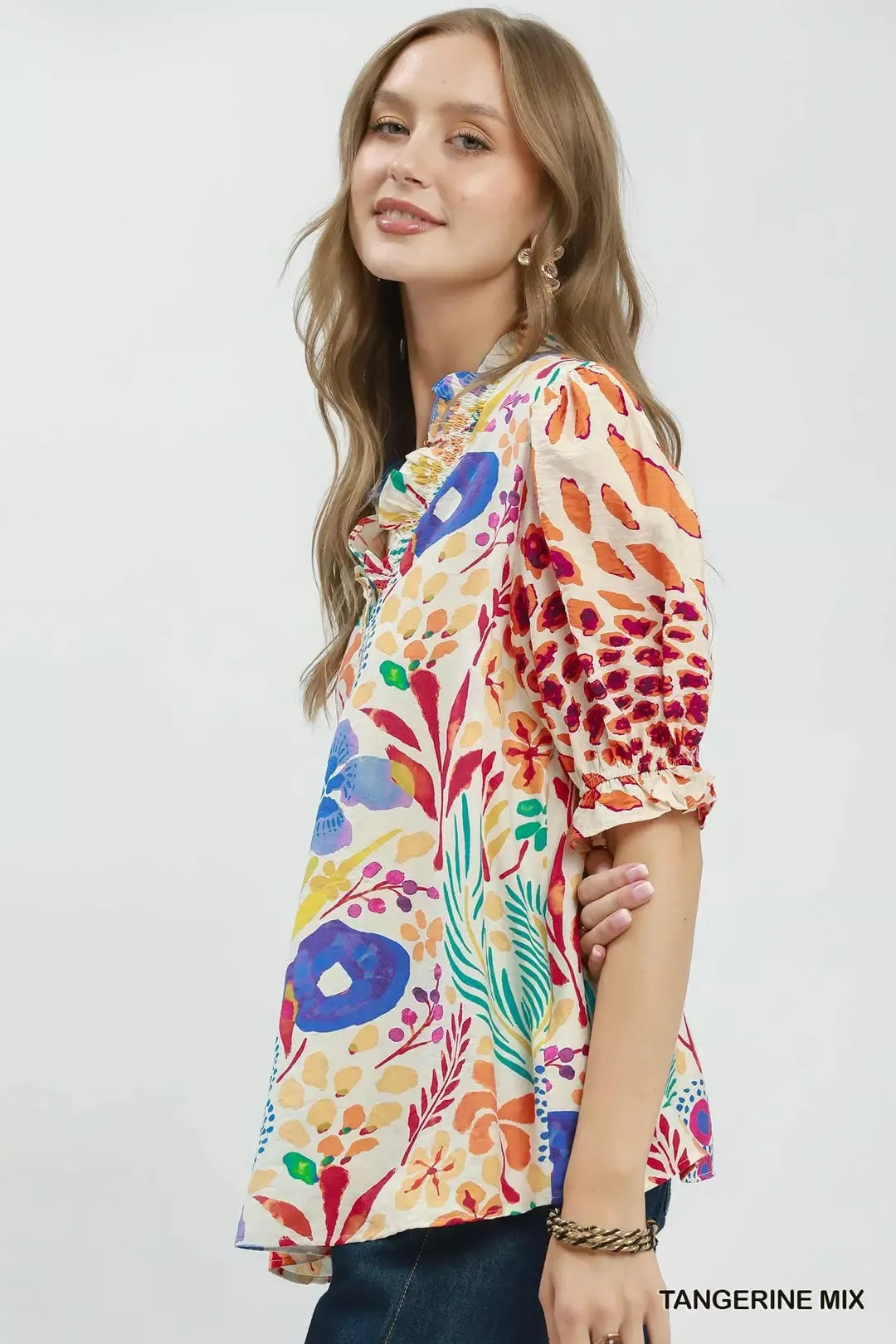 Colorful floral V-neck blouse with ruffle trim, puff sleeves, and a relaxed flowy fit styled with dark denim.