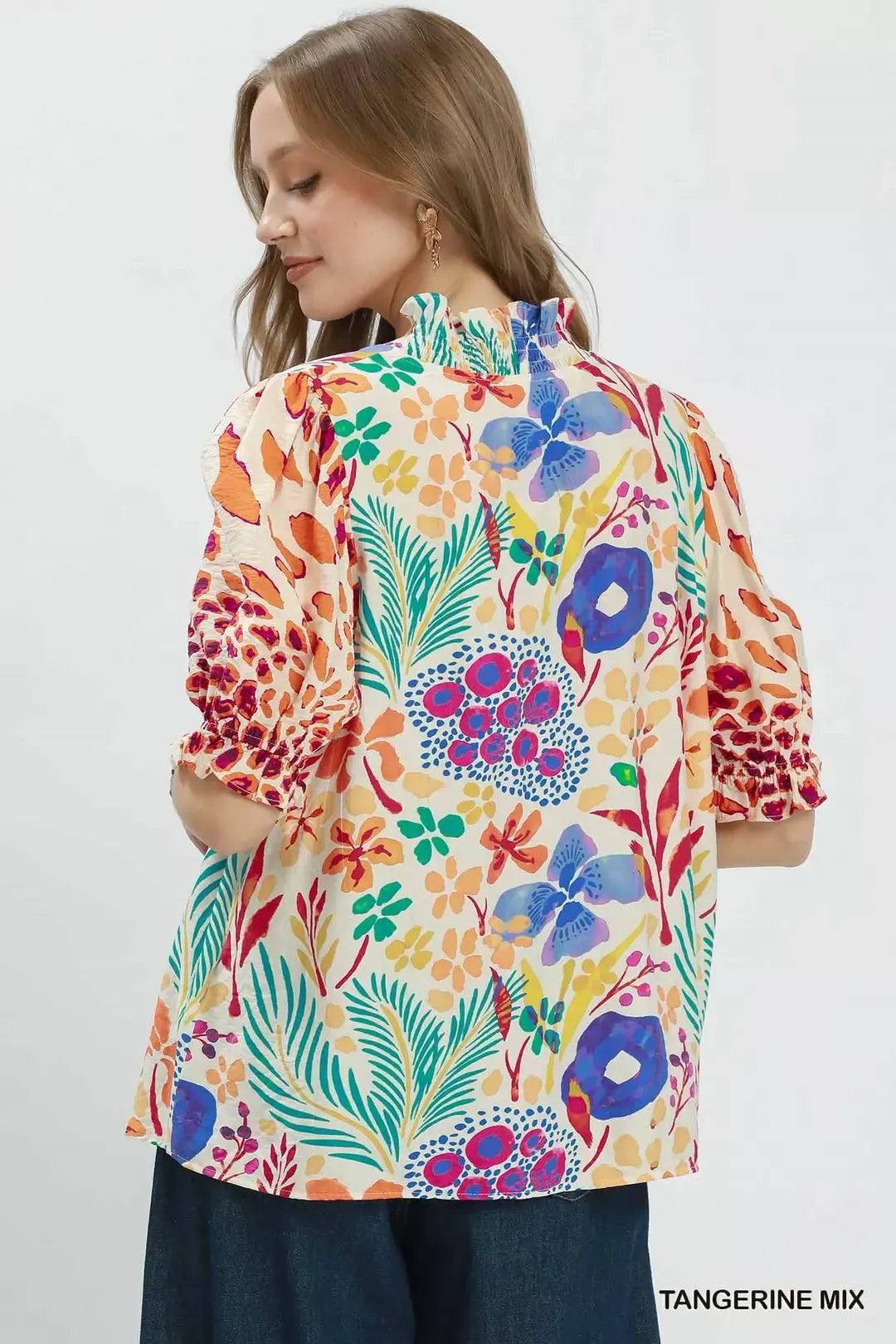 Colorful floral V-neck blouse with ruffle trim, puff sleeves, and a relaxed flowy fit styled with dark denim.