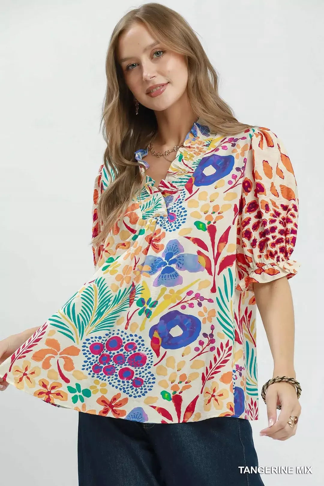 Colorful floral V-neck blouse with ruffle trim, puff sleeves, and a relaxed flowy fit styled with dark denim.