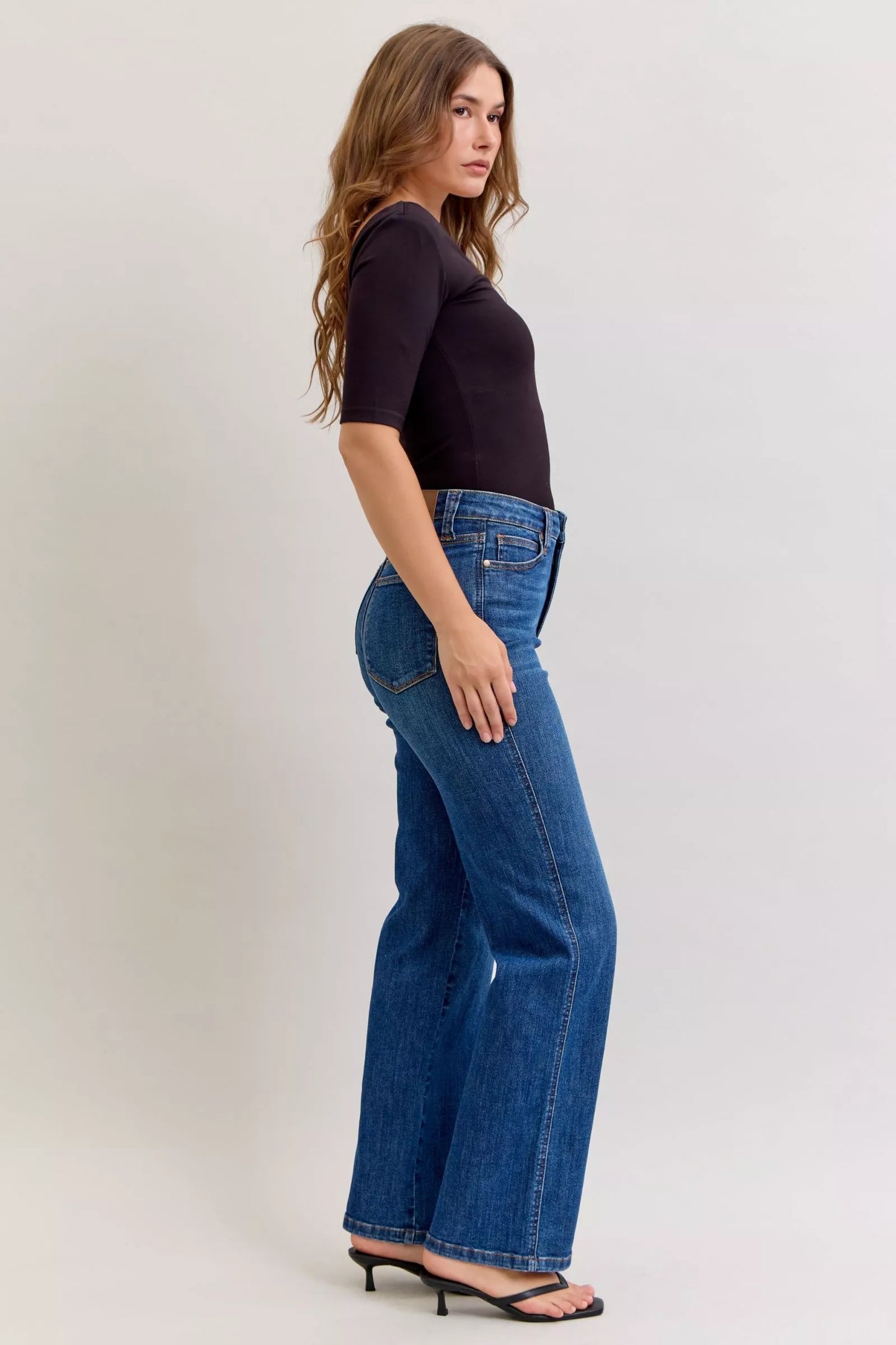 Model wearing dark wash high-rise straight jeans with tummy control fit, styled with a black top and sandals.