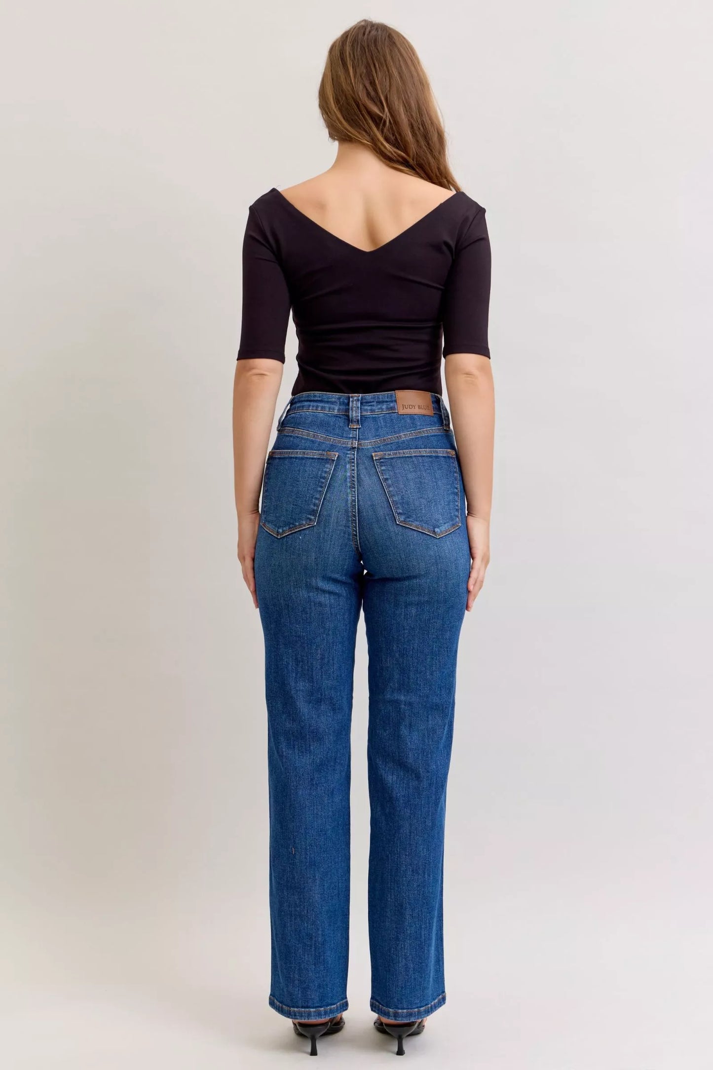 Model wearing dark wash high-rise straight jeans with tummy control fit, styled with a black top and sandals.