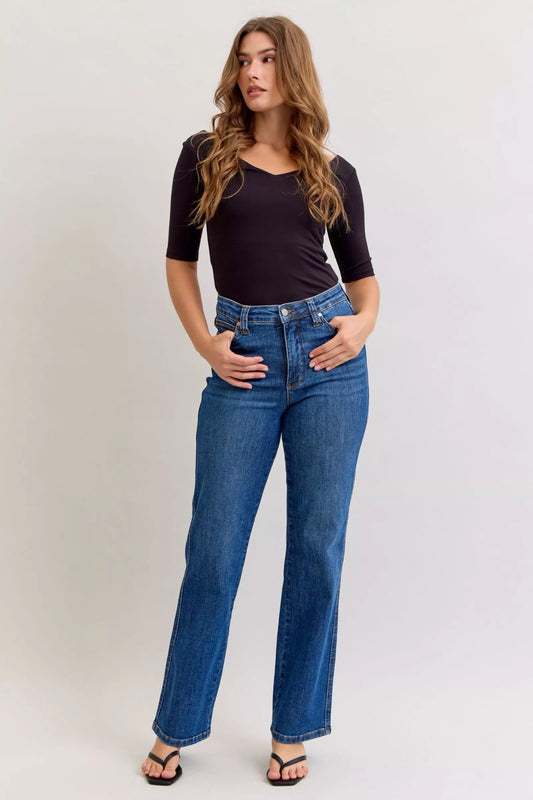 Model wearing dark wash high-rise straight jeans with tummy control fit, styled with a black top and sandals.