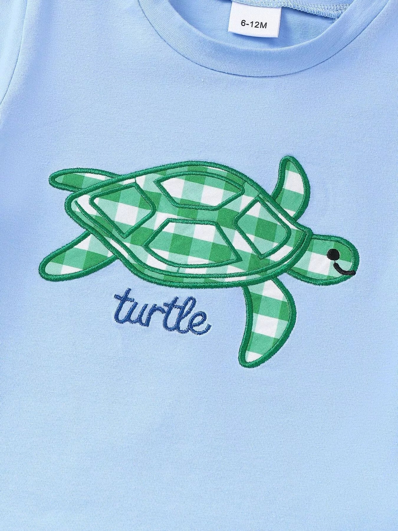 Two-piece baby outfit with blue turtle appliqué T-shirt and green gingham shorts made from a soft cotton-blend fabric.