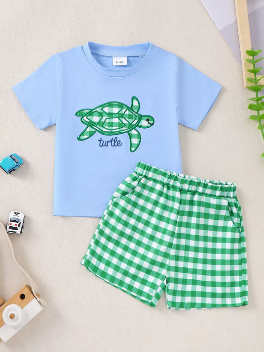 Two-piece baby outfit with blue turtle appliqué T-shirt and green gingham shorts made from a soft cotton-blend fabric.