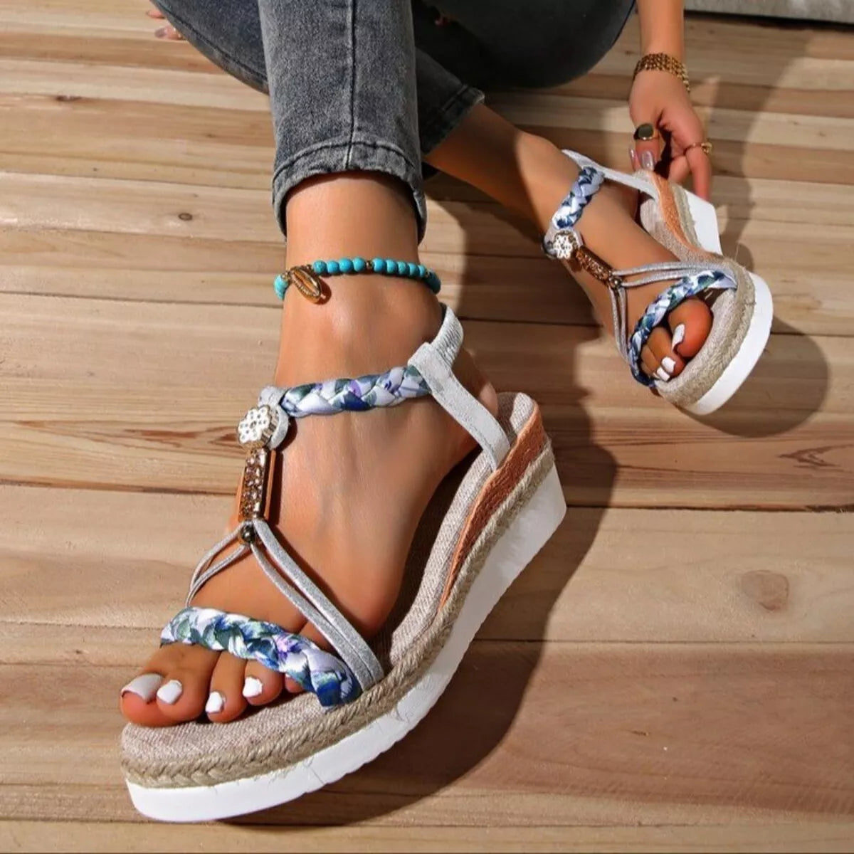 Boho open-toe wedge sandals with colorful braided straps, decorative charm details, low heel, and rubber sole styled with white pedicure.