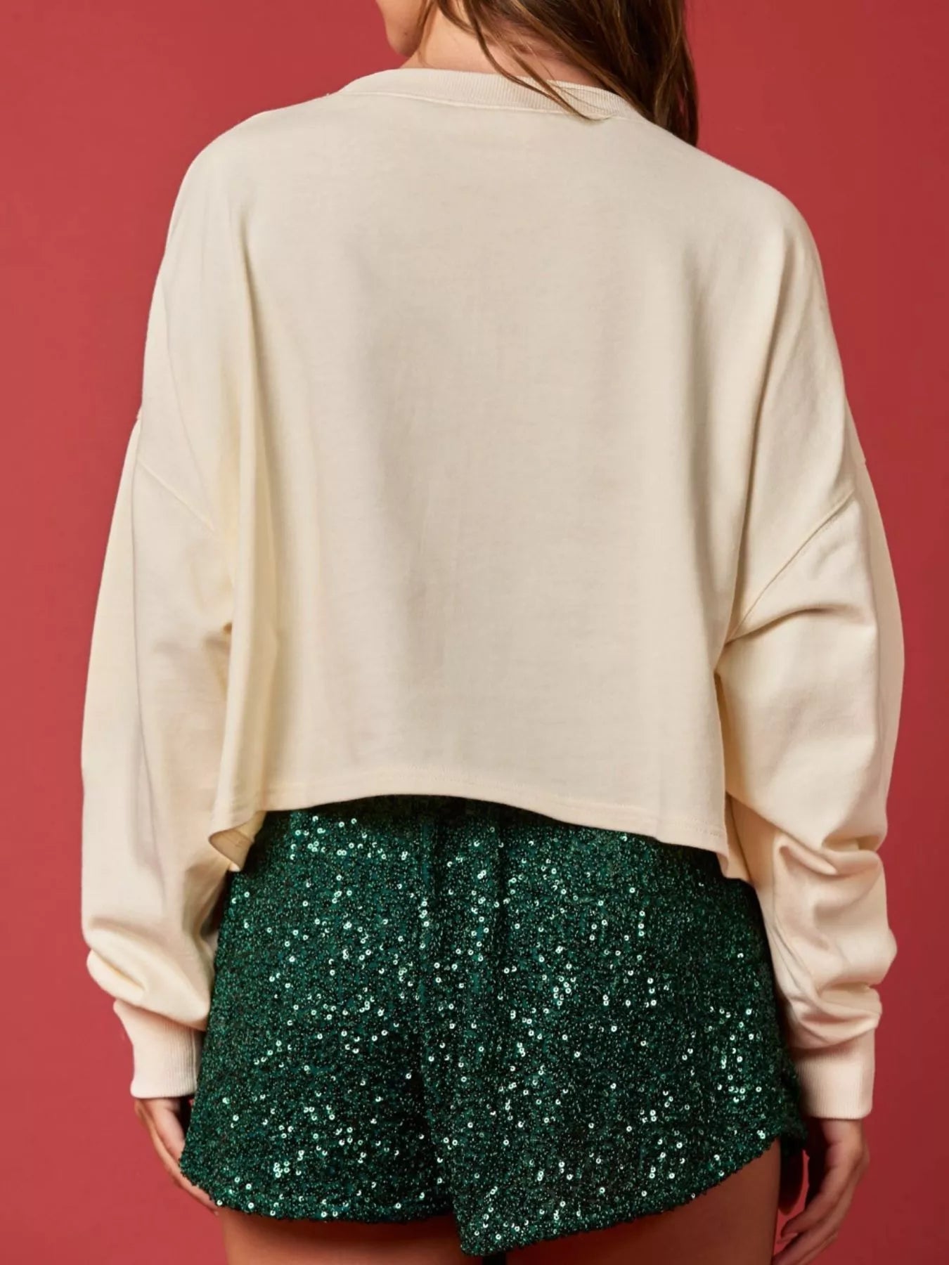 Woman wearing a cream sweatshirt with rainbow sequin Christmas lights and a sparkly green skirt — cheerful holiday outfit.