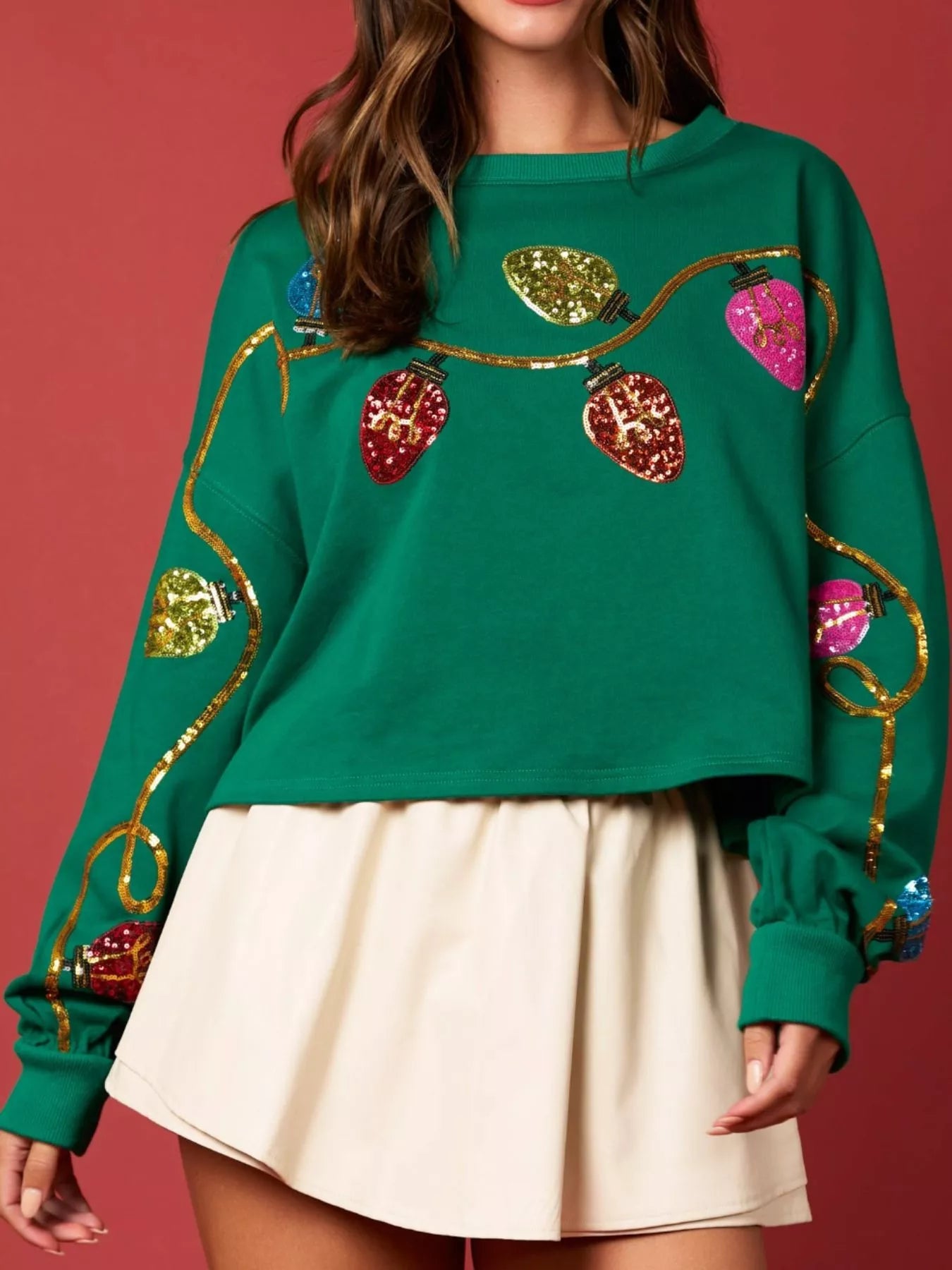 Woman wearing a green sweatshirt decorated with colorful sequin Christmas lights — festive holiday top from A Whimsical Affair.
