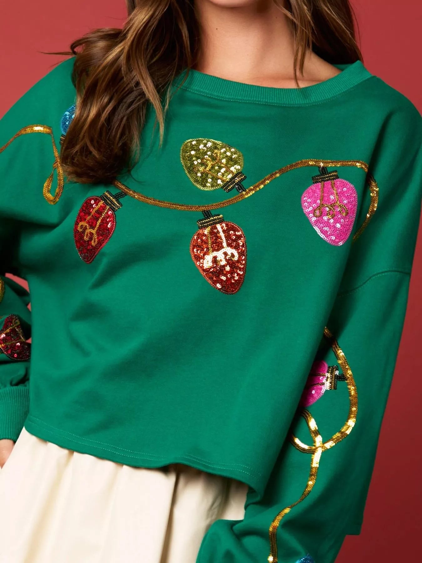 Woman wearing a green sweatshirt decorated with colorful sequin Christmas lights — festive holiday top from A Whimsical Affair.