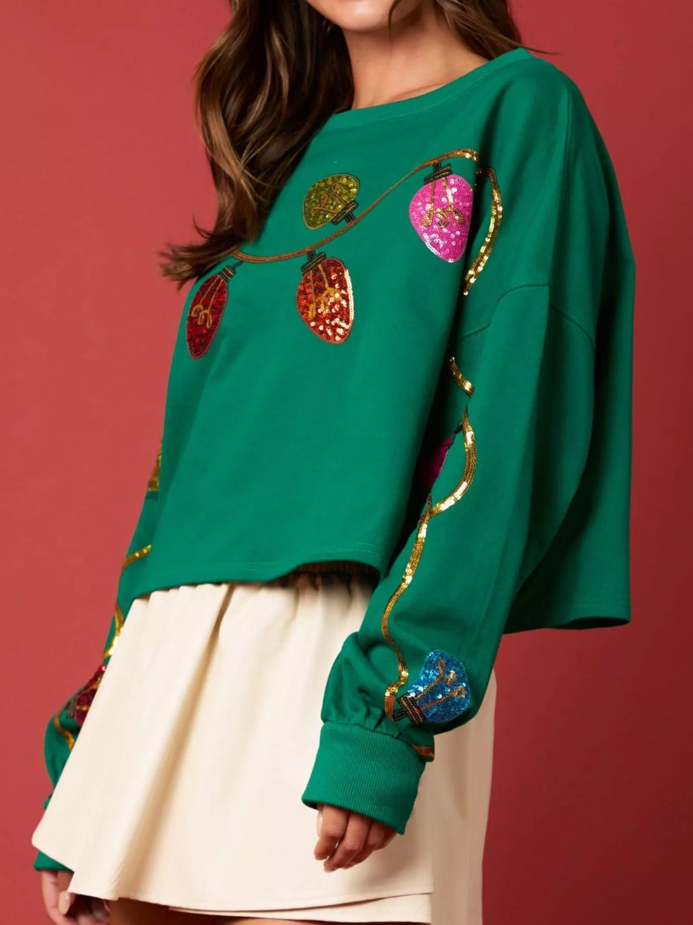 Woman wearing a green sweatshirt decorated with colorful sequin Christmas lights — festive holiday top from A Whimsical Affair.