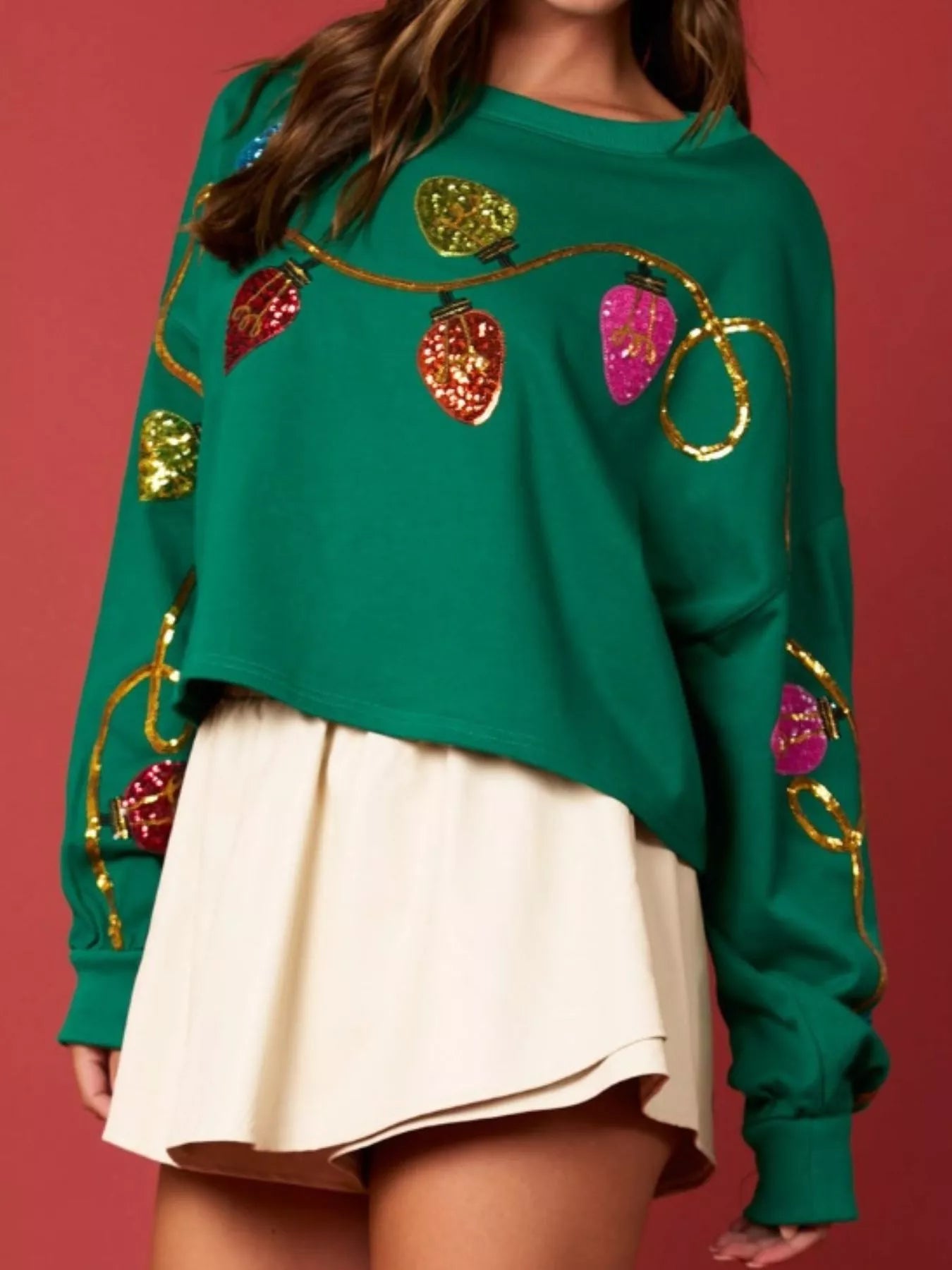 Woman wearing a green sweatshirt decorated with colorful sequin Christmas lights — festive holiday top from A Whimsical Affair.