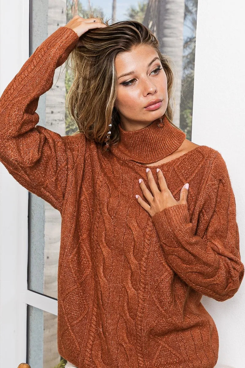 Woman wearing a rust-colored cable knit sweater with mock neck and cold shoulder cutout