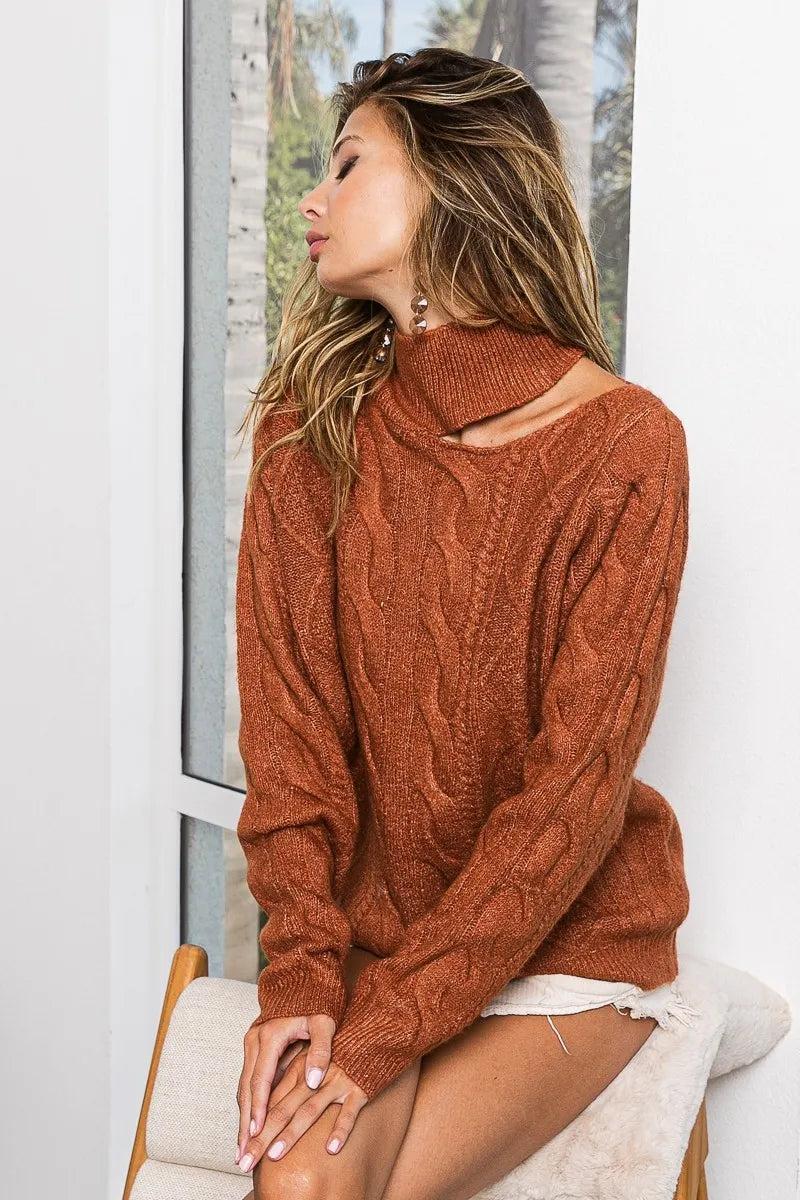 Woman wearing a rust-colored cable knit sweater with mock neck and cold shoulder cutout
